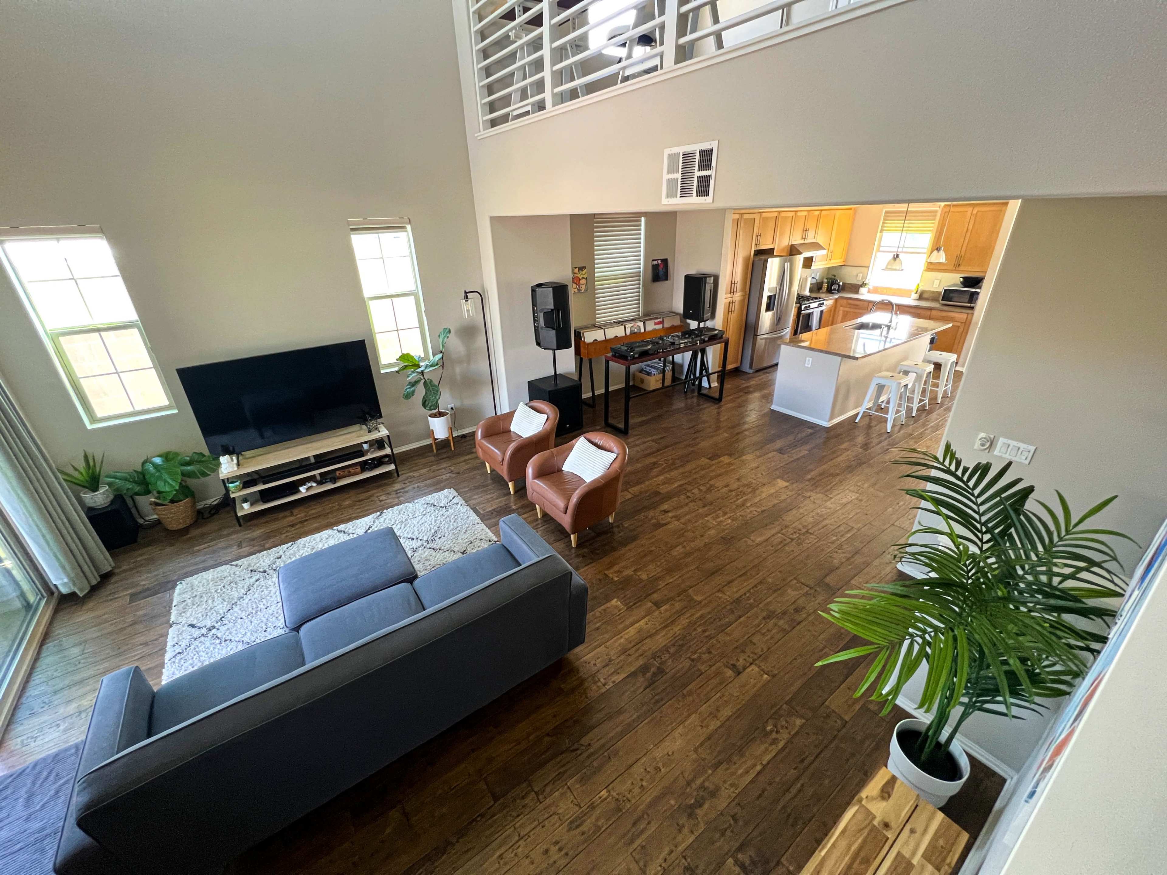 A spacious living room with a grey sofa, two brown chairs, a television, and an open kitchen area in the background.