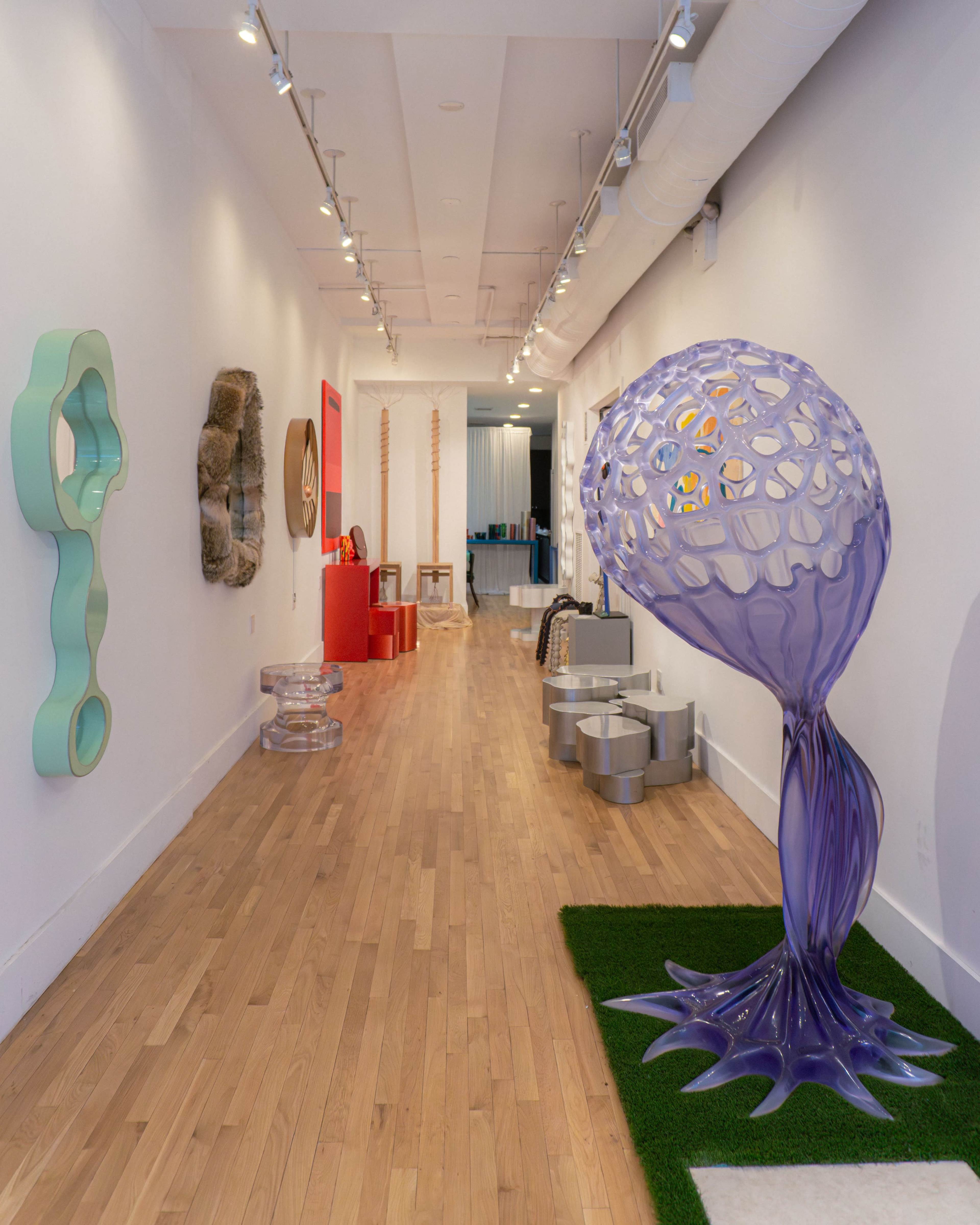 The image shows a spacious art gallery featuring various modern sculptures and artwork along the walls and a unique purple sculptural piece in the foreground.