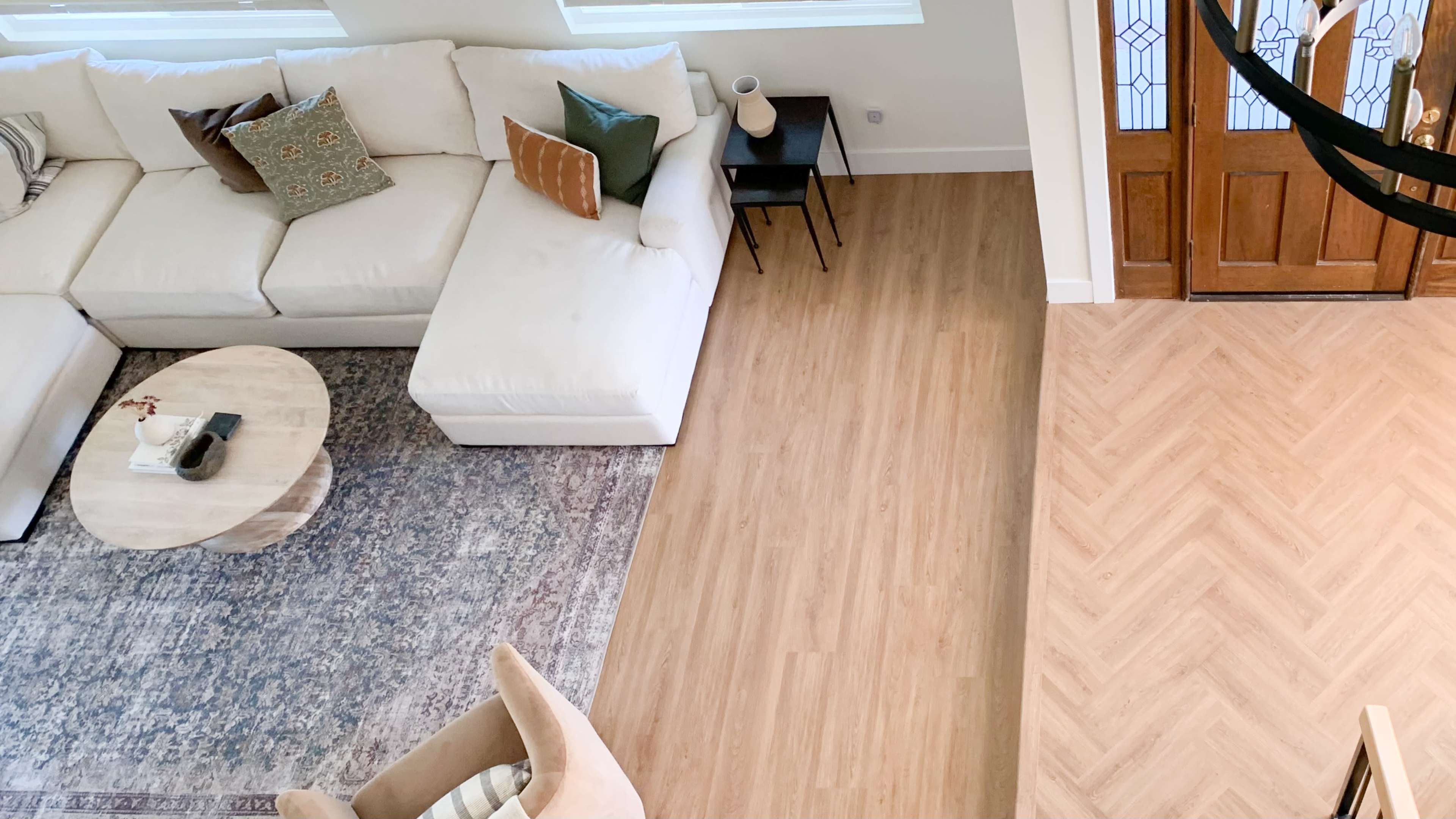 A spacious living area with a sectional sofa, a round coffee table, a patterned rug, and an entrance featuring wooden double doors.