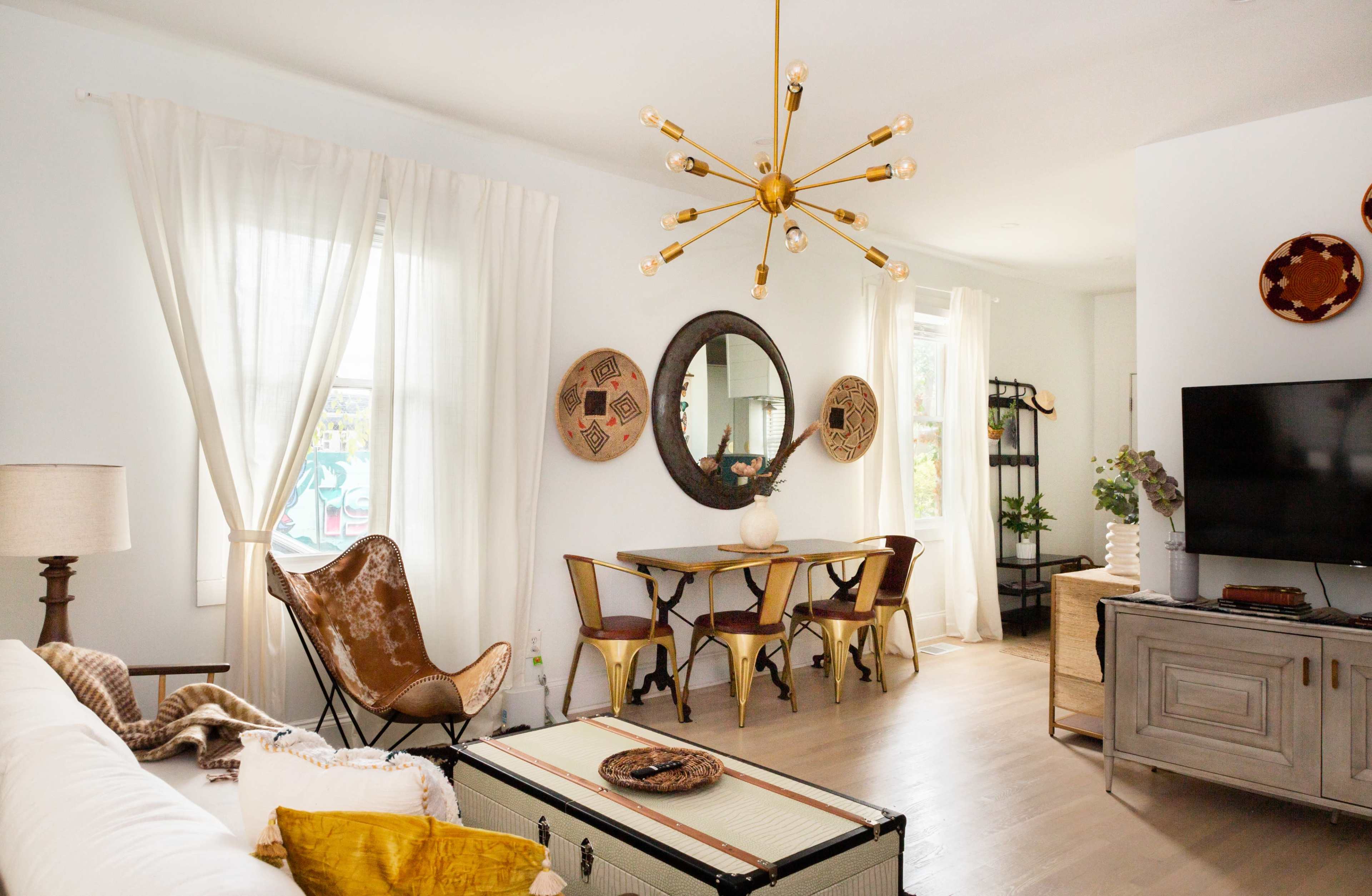 The living space features a light-filled room with a sofa, a dining table, decorative wall mirrors, and a distinctive light fixture.
