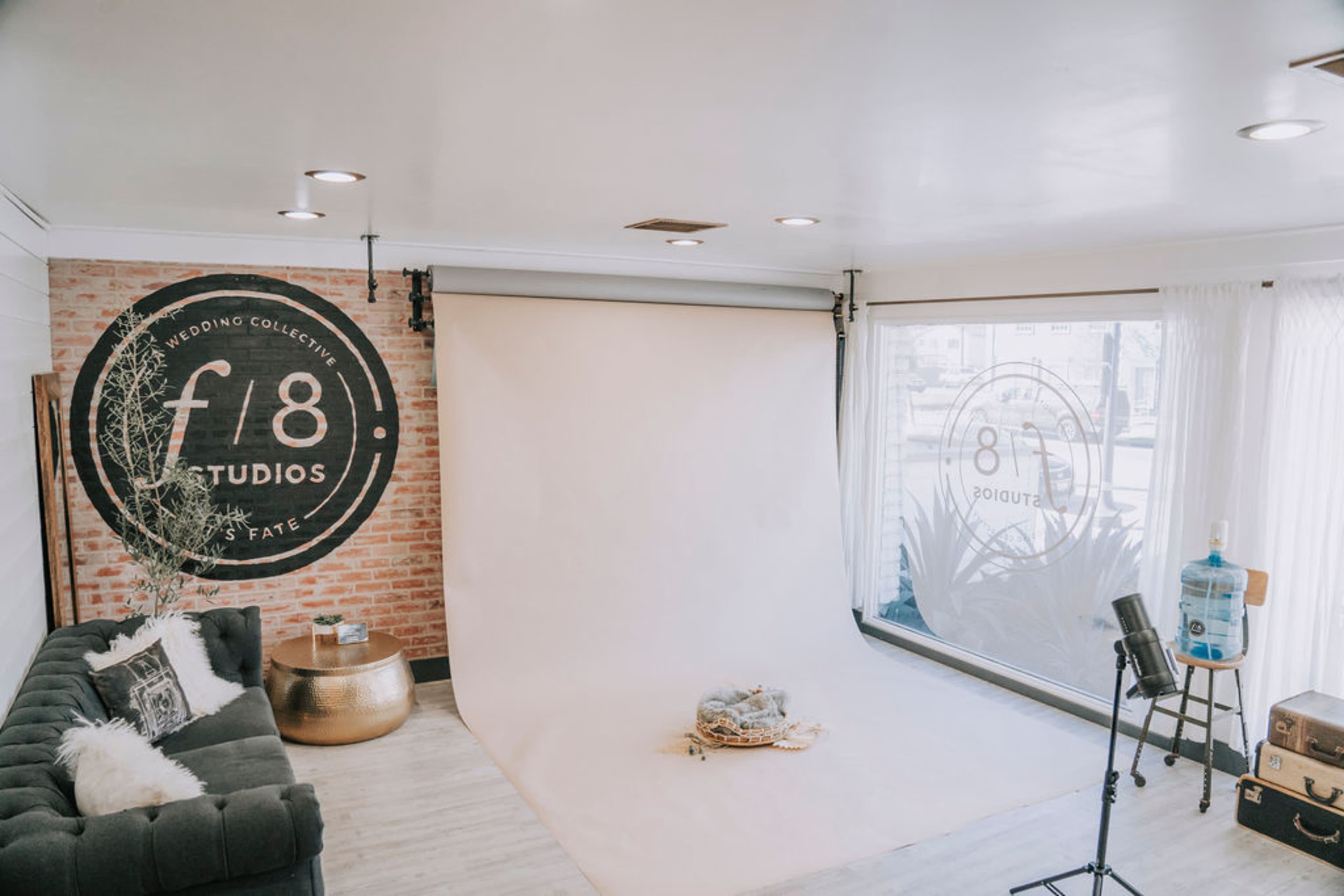 A photography studio with a white backdrop, a black sofa, and branding on the walls, including a large circular logo.