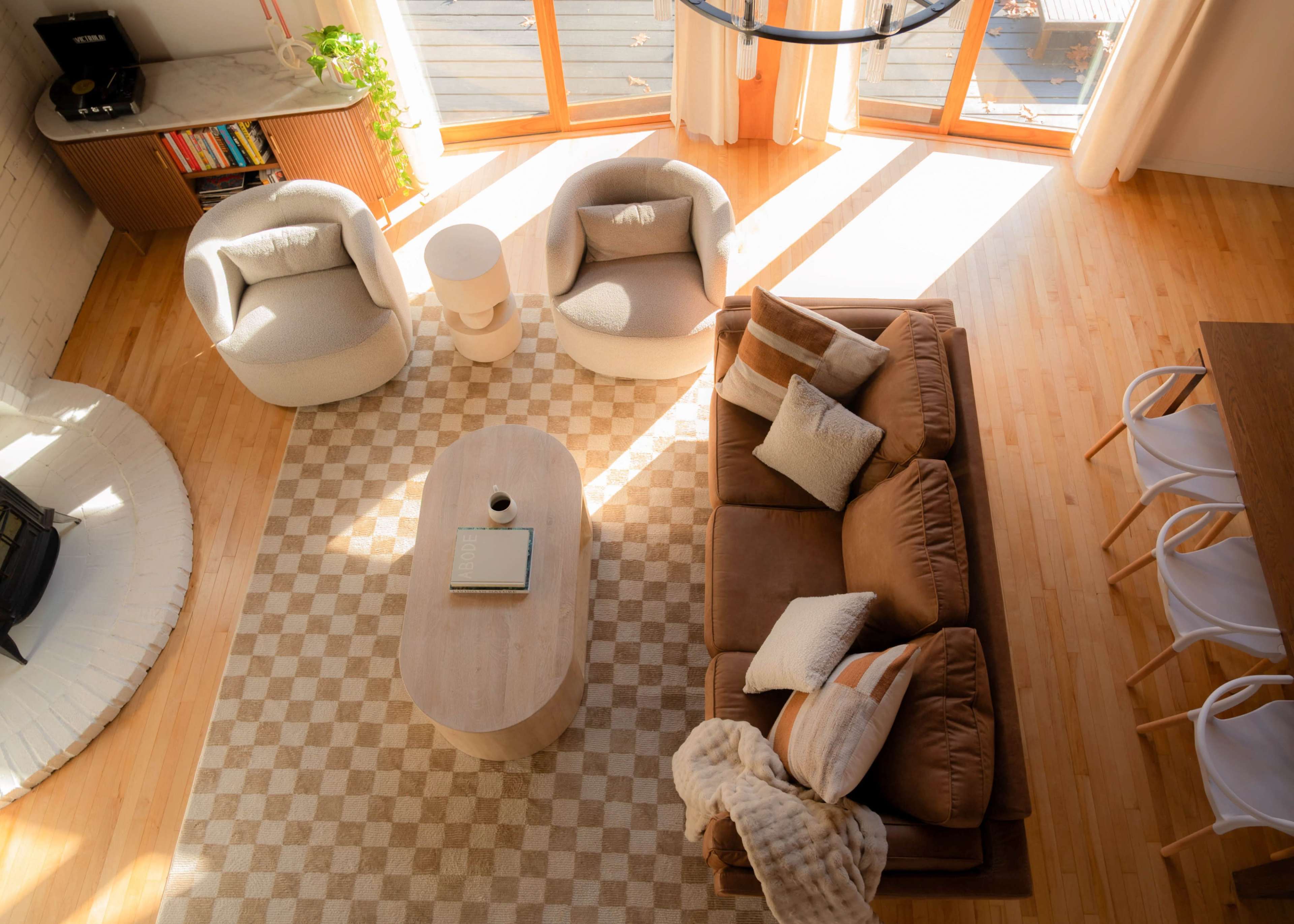 A bright, modern living room with two armchairs, a coffee table, and a brown sofa arranged on a patterned rug.