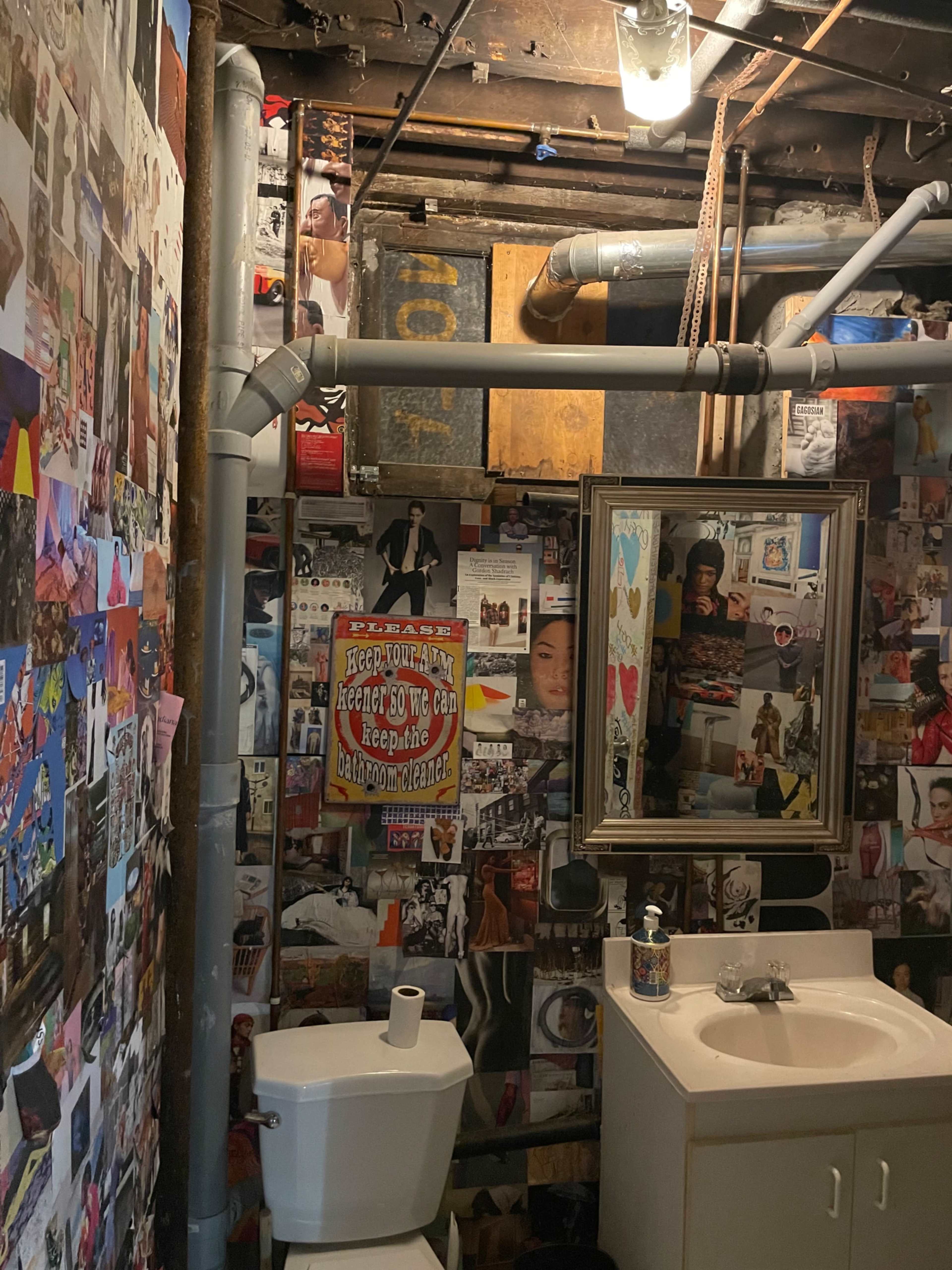 The image shows a small bathroom with walls covered in a collage of various photographs and artworks, alongside a toilet and a sink with a mirror.