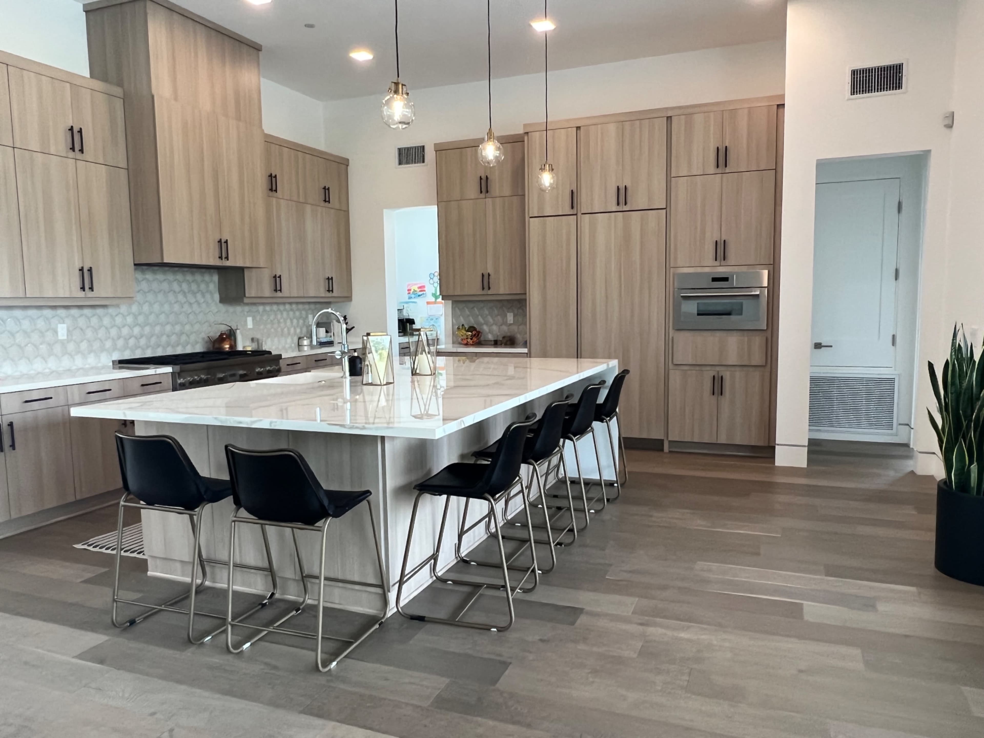 A modern kitchen features a large island with seating for six, surrounded by wood cabinetry and stainless steel appliances.