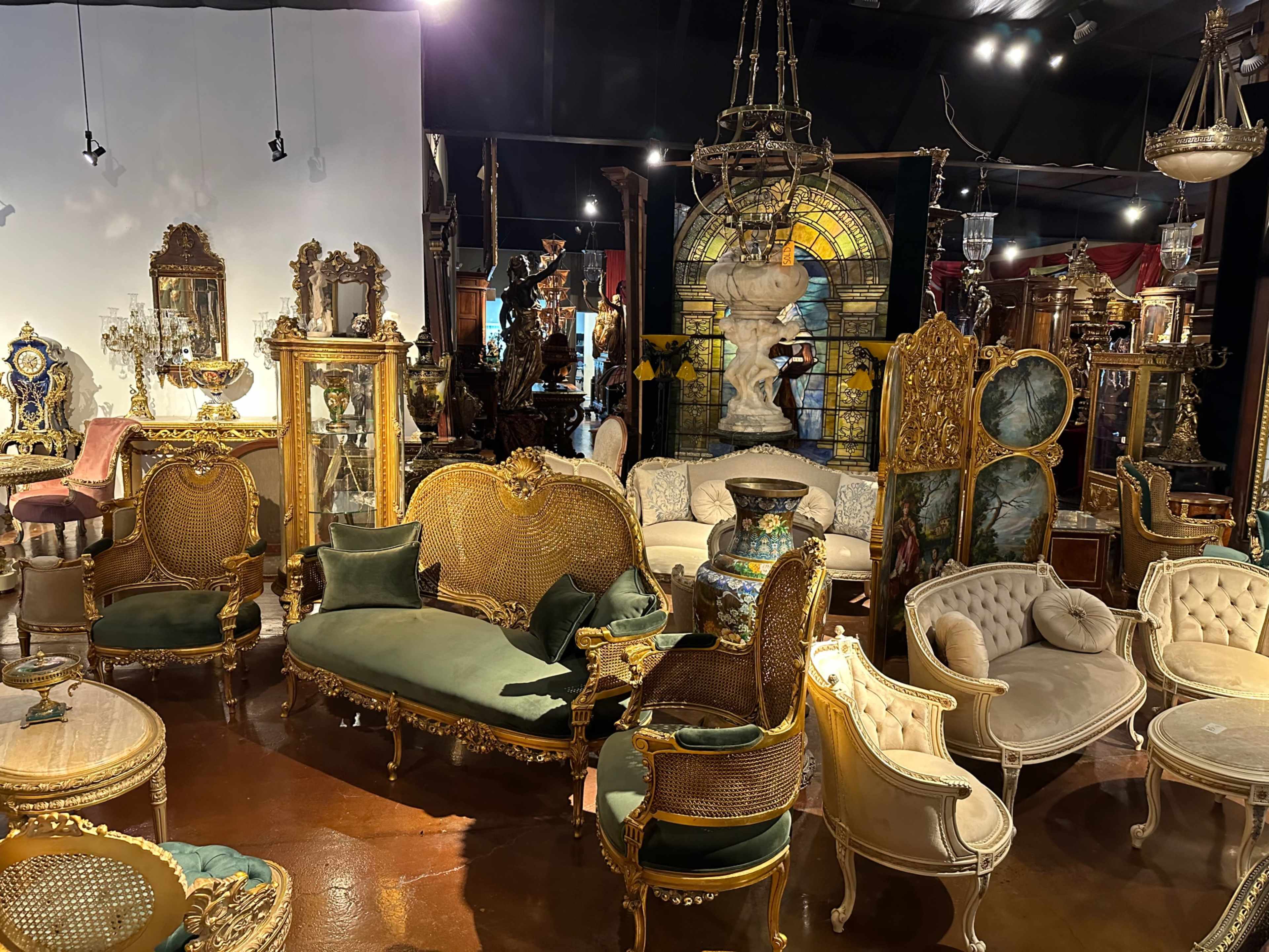 A vintage furniture store filled with ornate chairs, sofas, and decorative mirrors arranged around a stained glass feature.