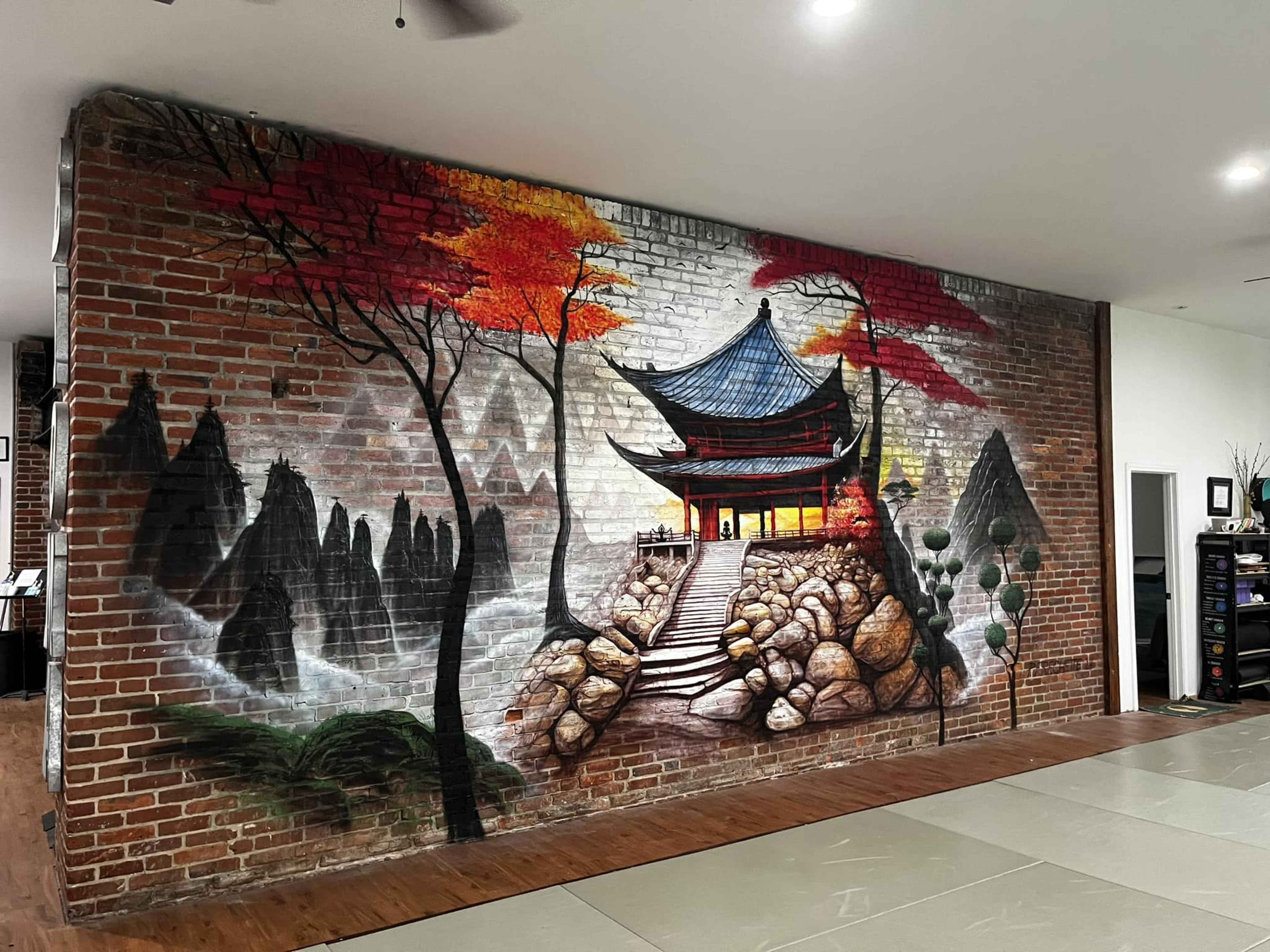 The image features a mural of a traditional Chinese pavilion set against a backdrop of mountains and trees, painted on a brick wall.