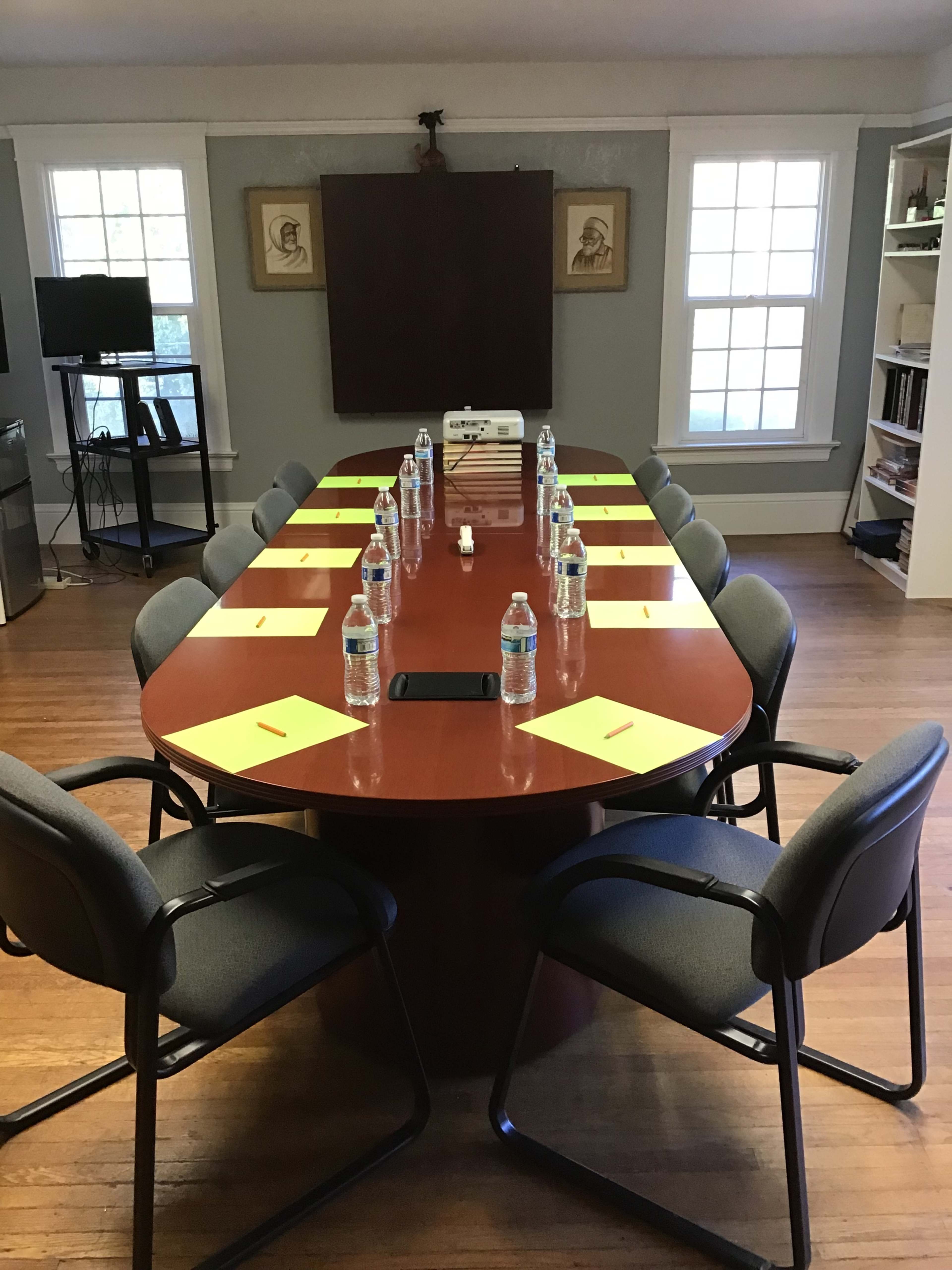 A long conference table is set with water bottles and notepads, surrounded by chairs in a well-lit room.