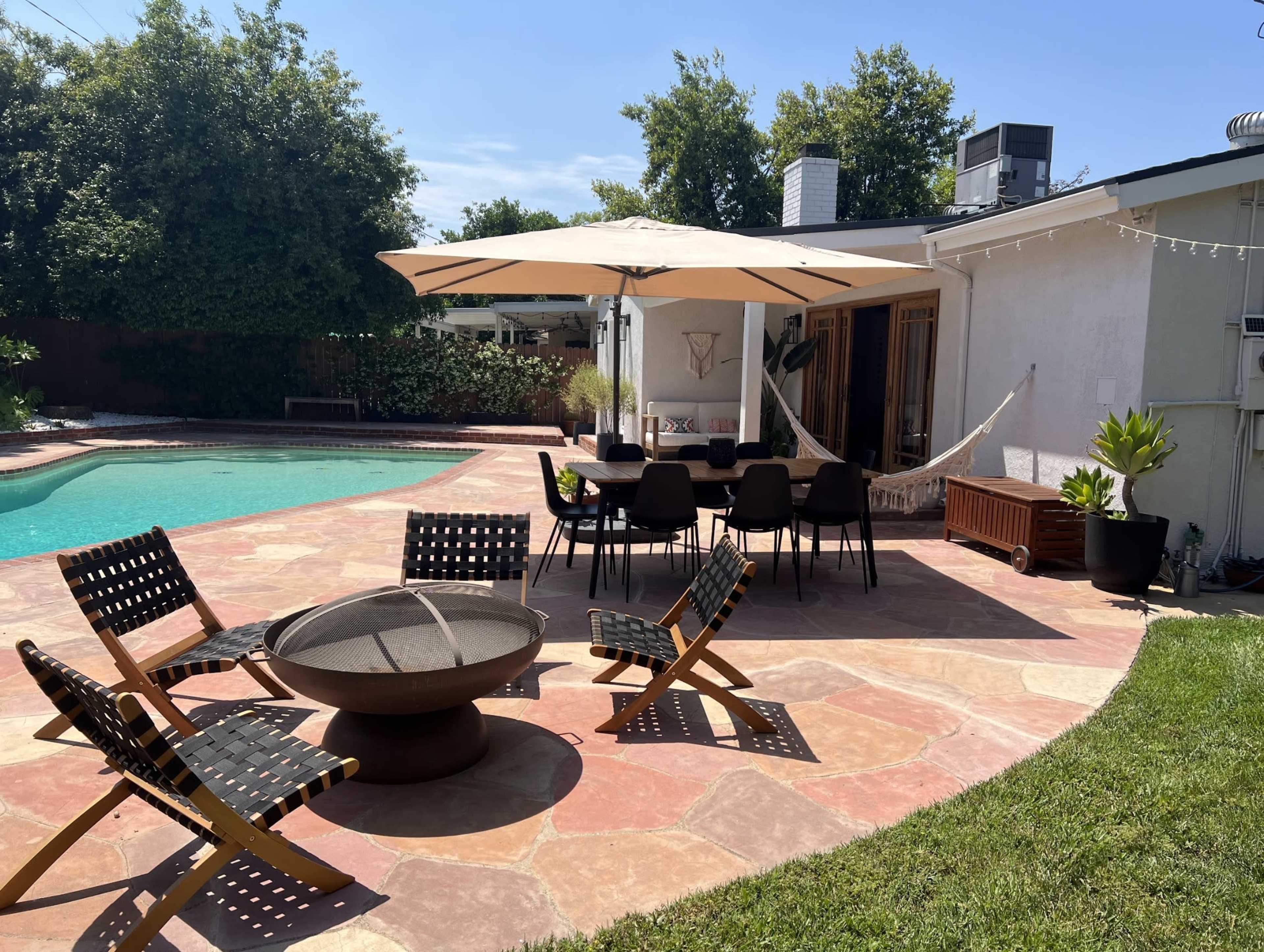 A backyard features a swimming pool, patio seating with a fire pit, and a hammock under an umbrella.