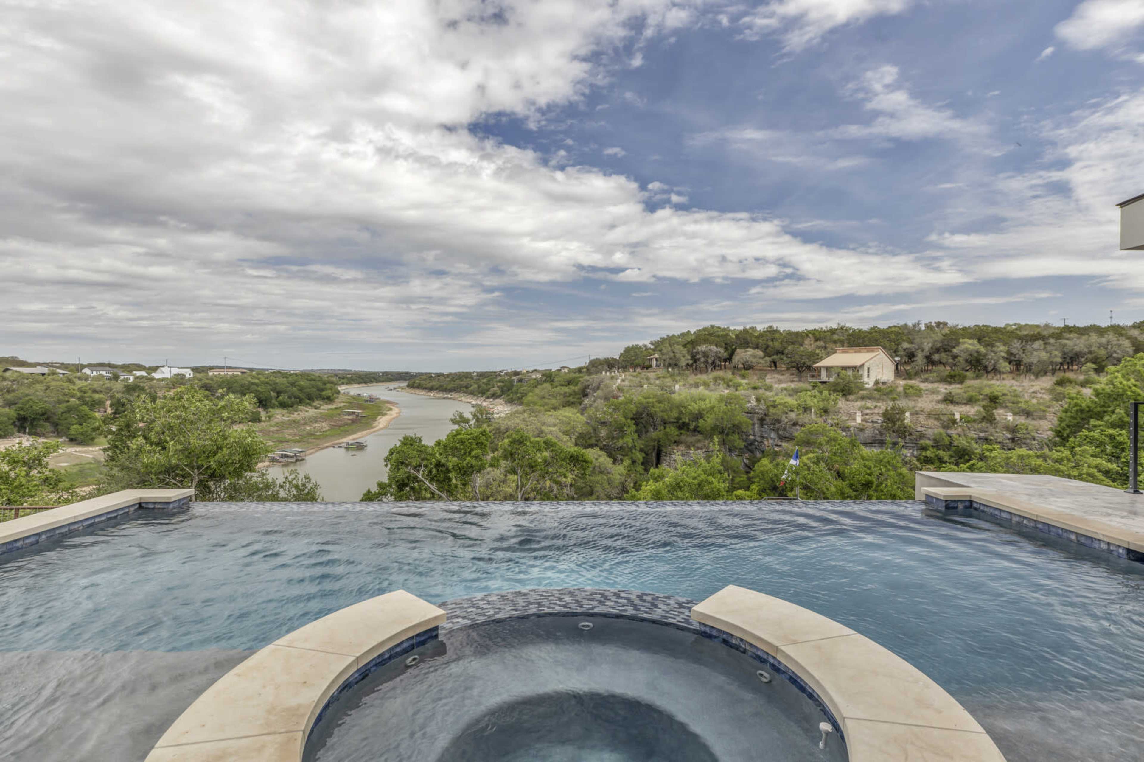 An infinity pool overlooks a winding river surrounded by lush greenery under a cloudy sky.