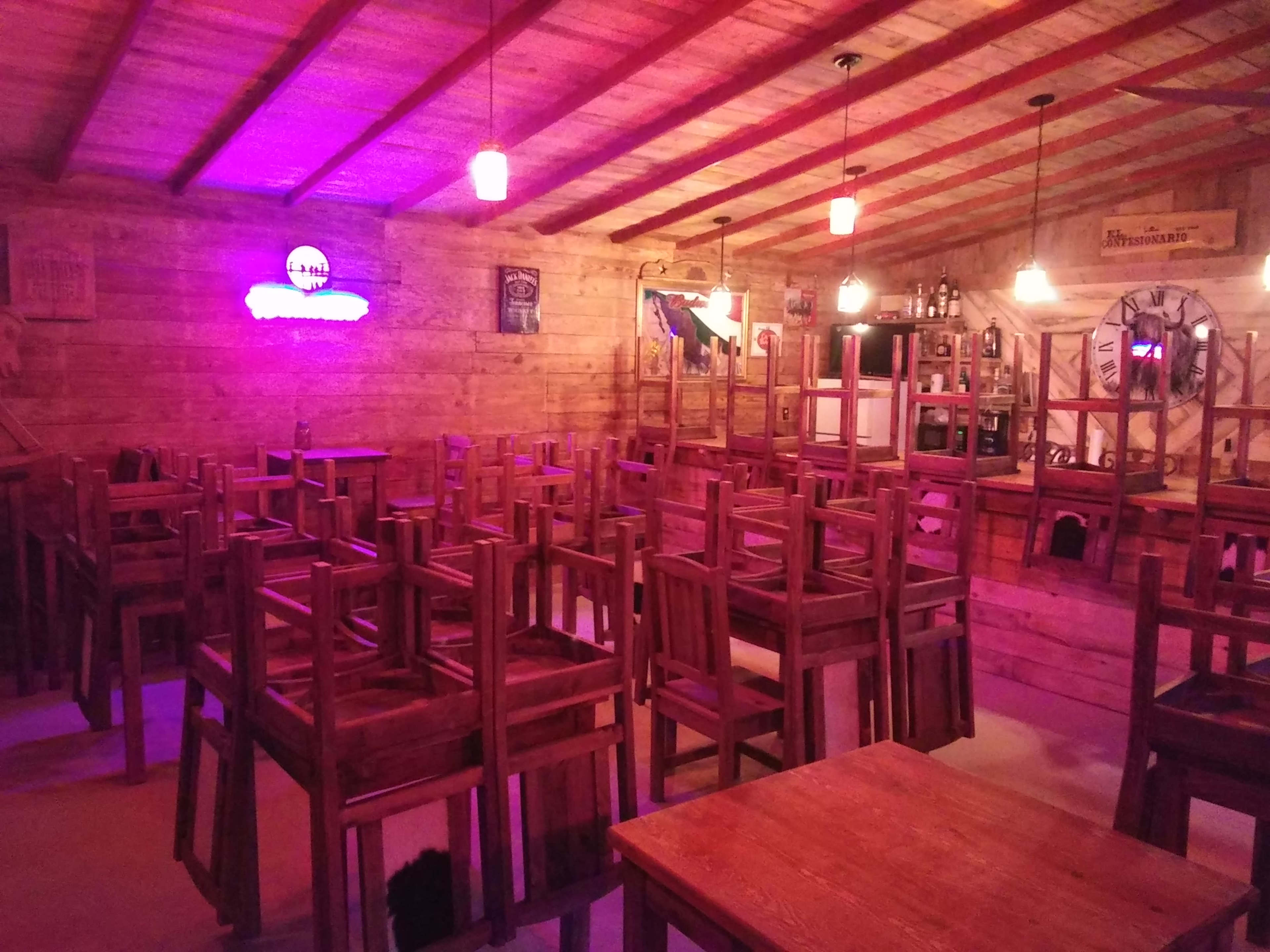 An interior view of a rustic wooden restaurant with tables stacked upside down and chairs piled on top in a dimly lit space.