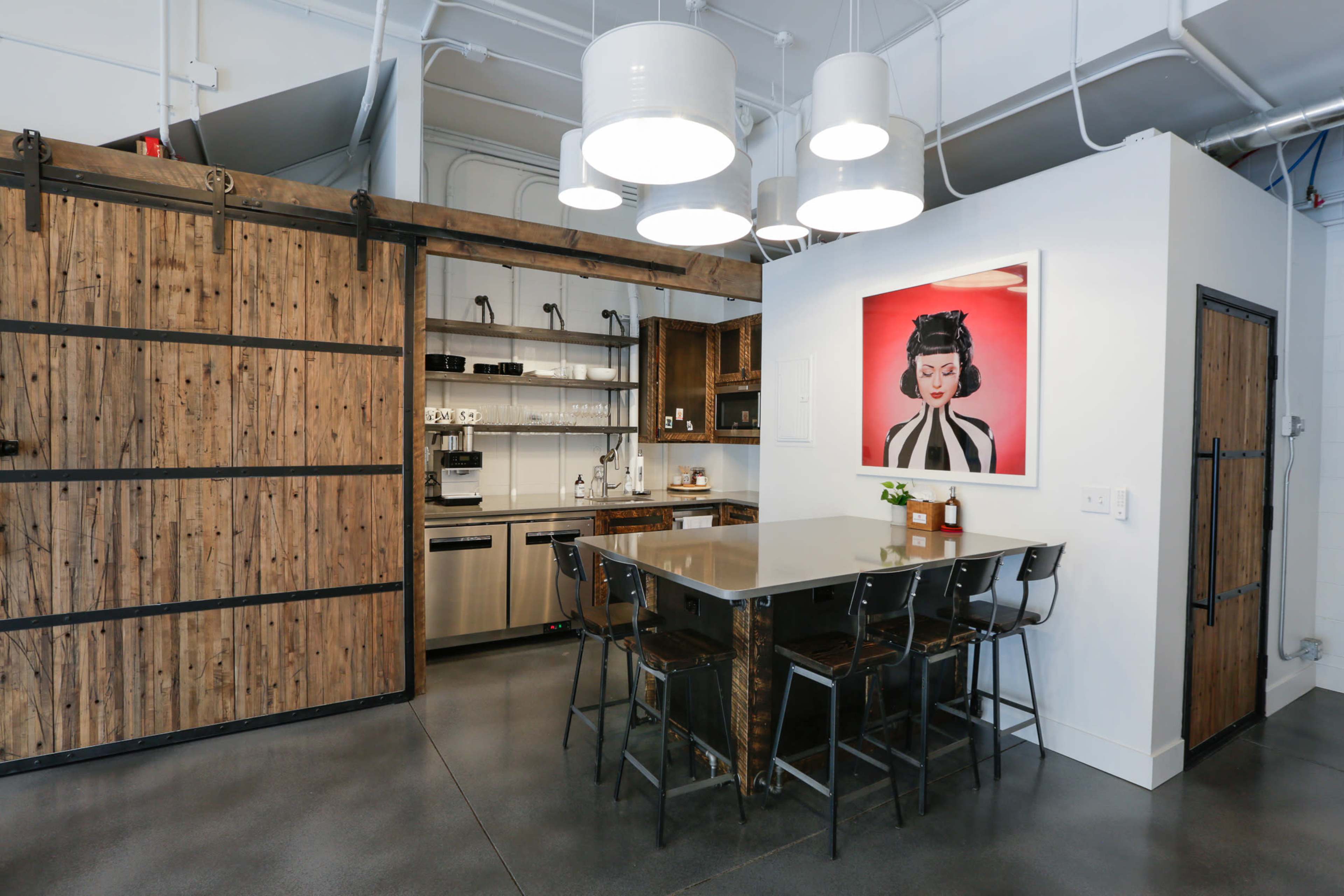 A modern kitchen featuring a wooden sliding barn door, stainless steel appliances, a gray countertop with bar stools, and a framed artwork on the wall.