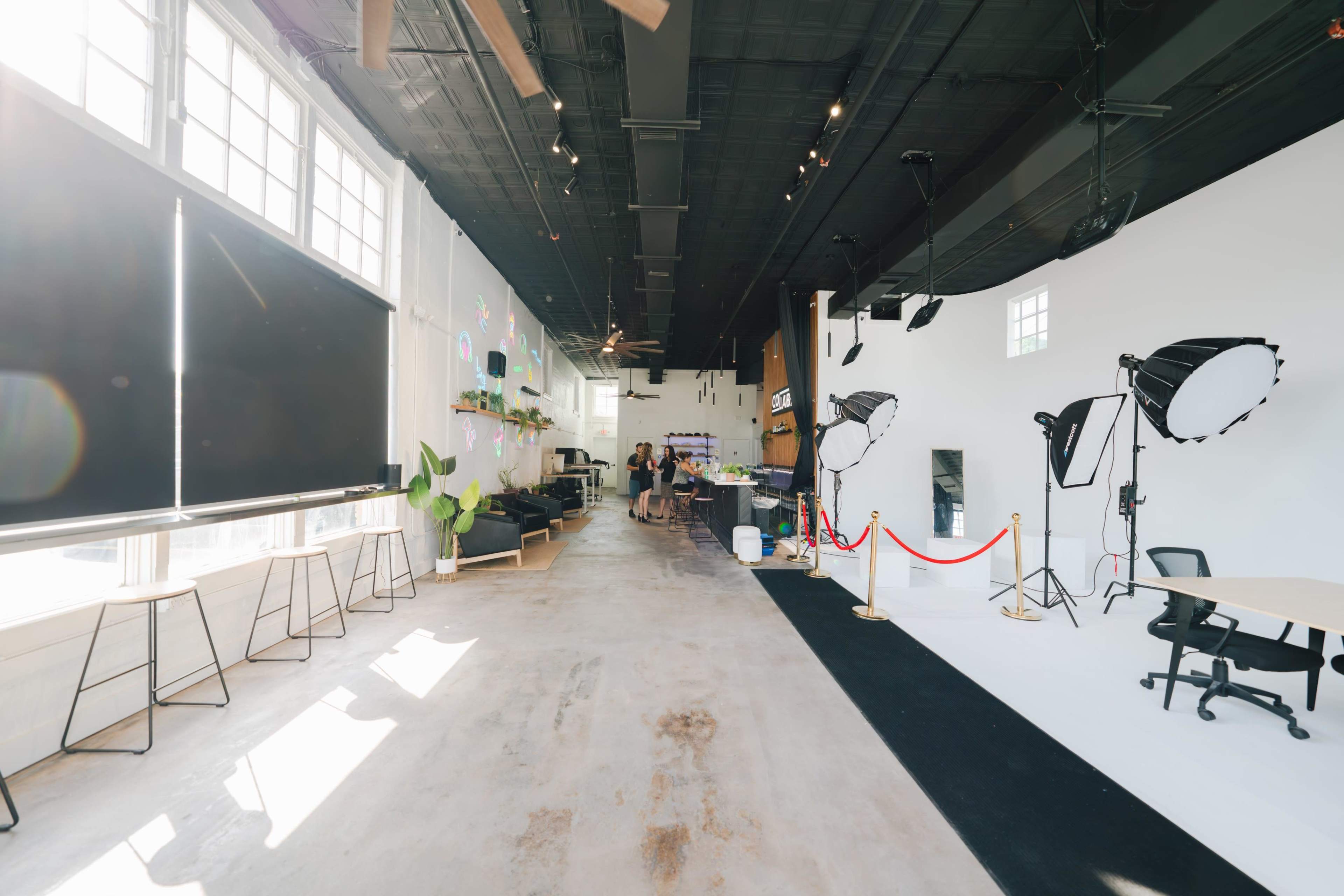 A spacious studio area with large windows, featuring seating, plants, and professional lighting equipment arranged for photo shoots.