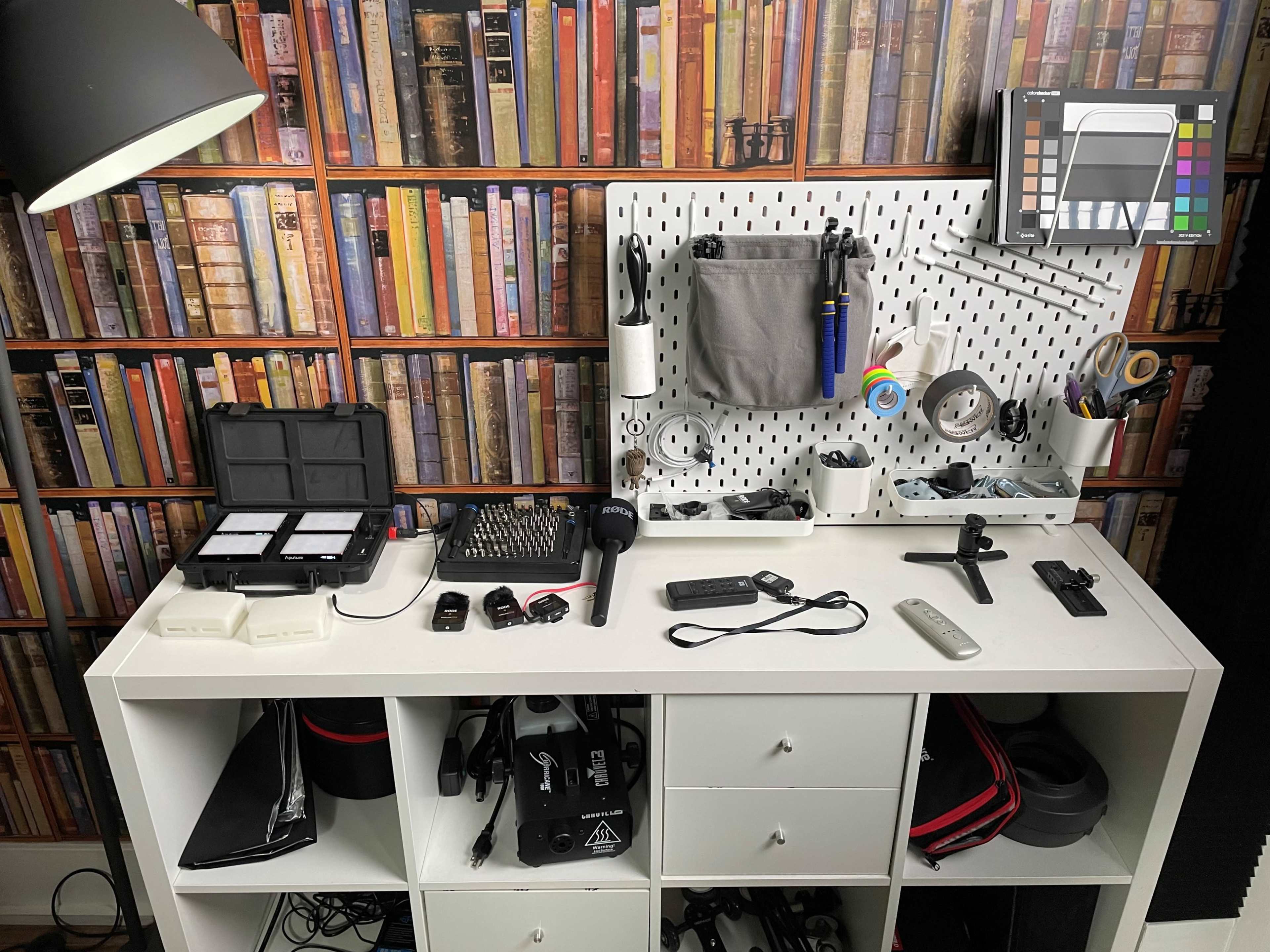 A well-organized workspace features tools, a keyboard, and storage on a white shelf against a backdrop of colorful, stacked books.