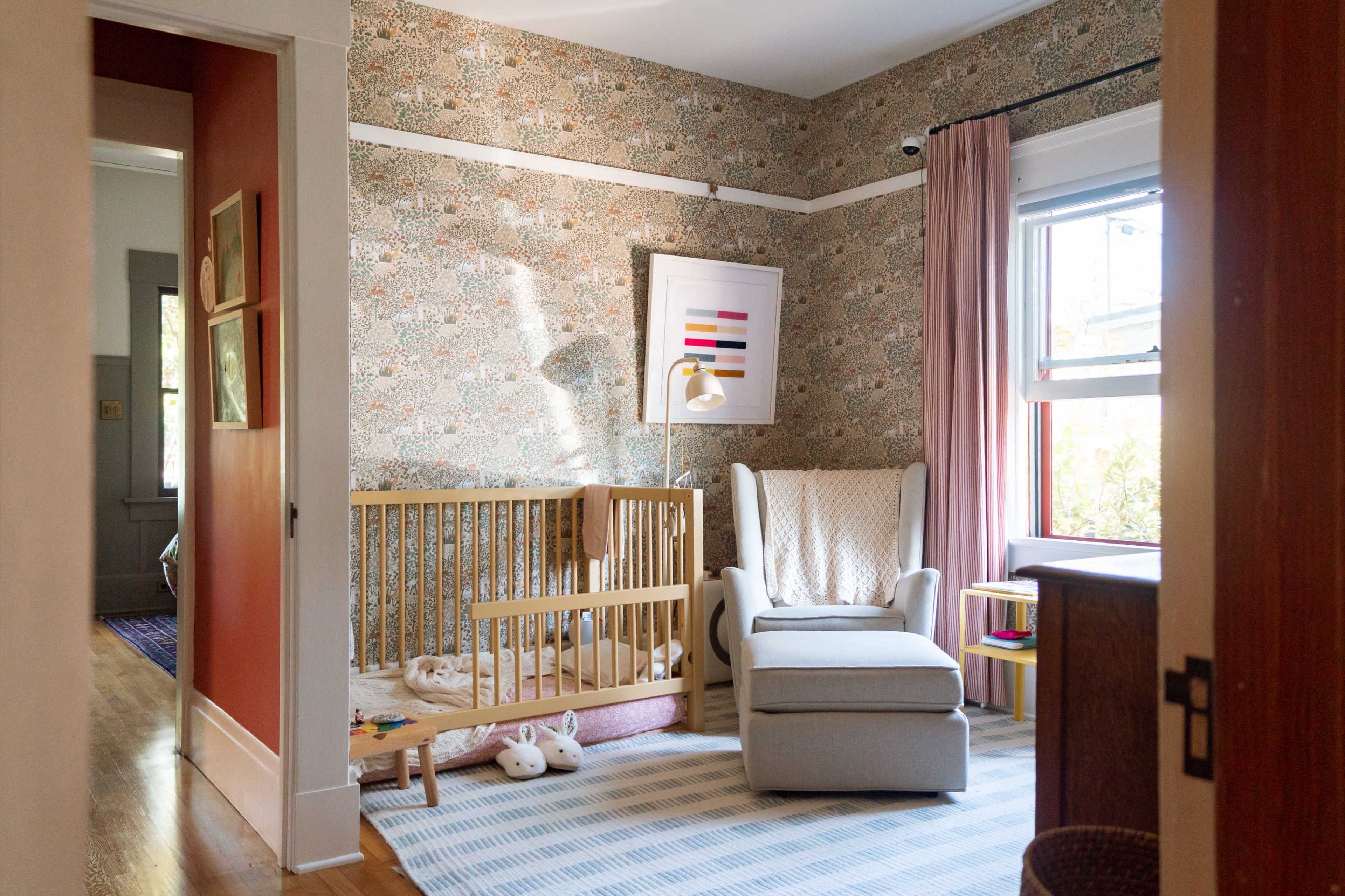 The image depicts a cozy nursery with a crib, a plush armchair, and patterned wallpaper.