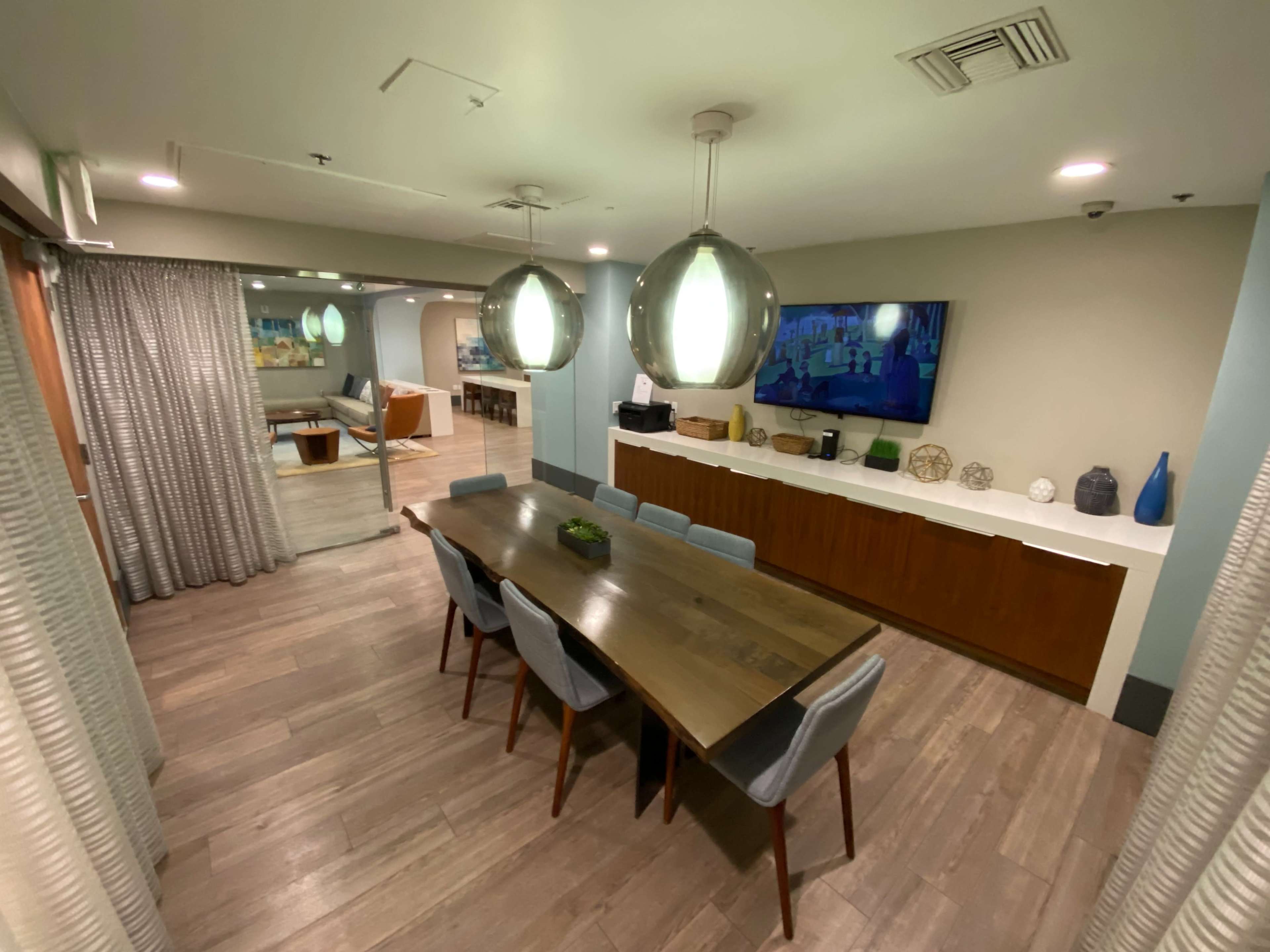A modern dining area with a wooden table surrounded by gray chairs, a long sideboard against the wall, and pendant lights hanging from the ceiling.
