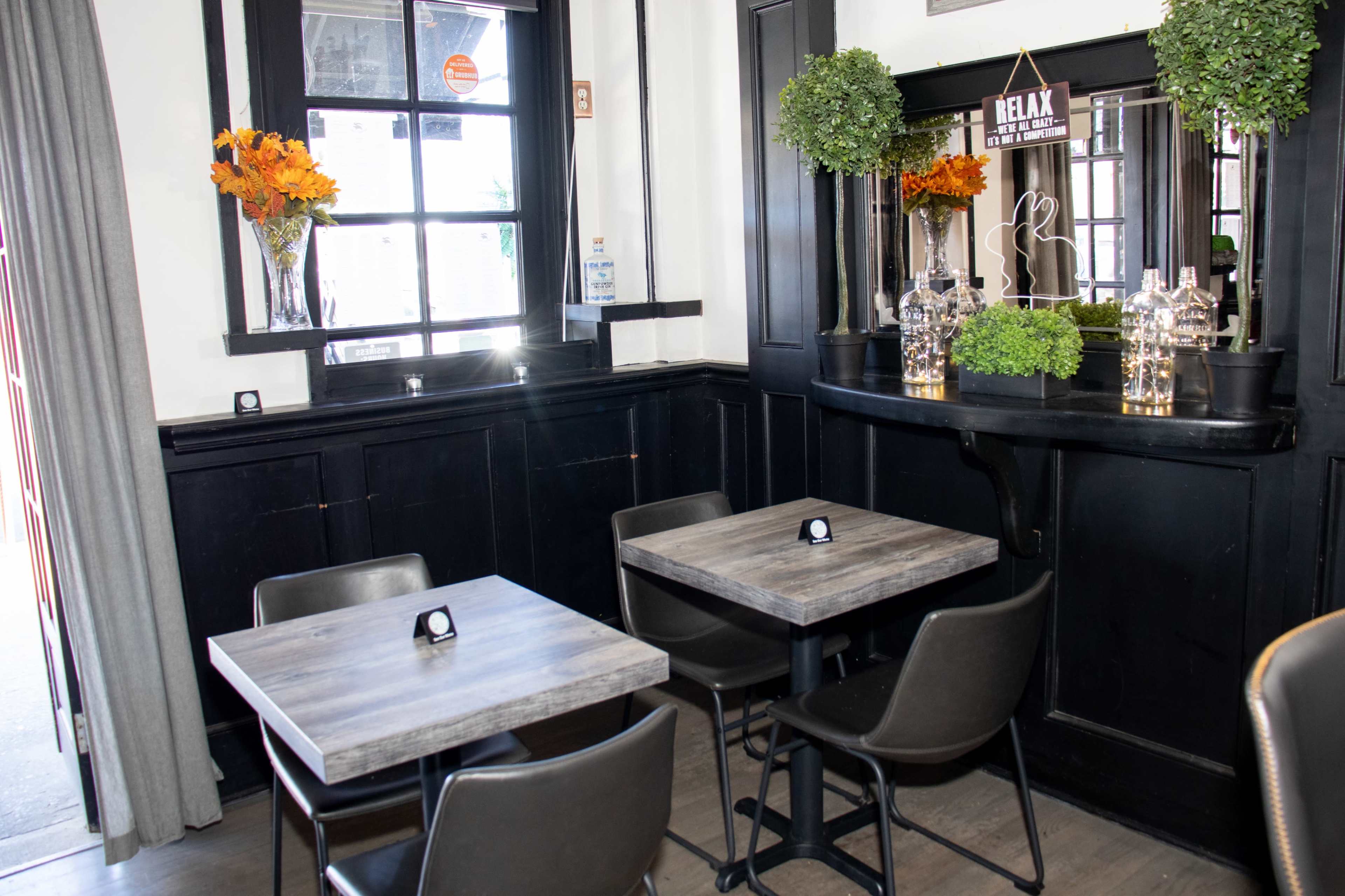 A cozy restaurant interior with wooden tables and chairs, framed by dark walls and large windows decorated with flowers.