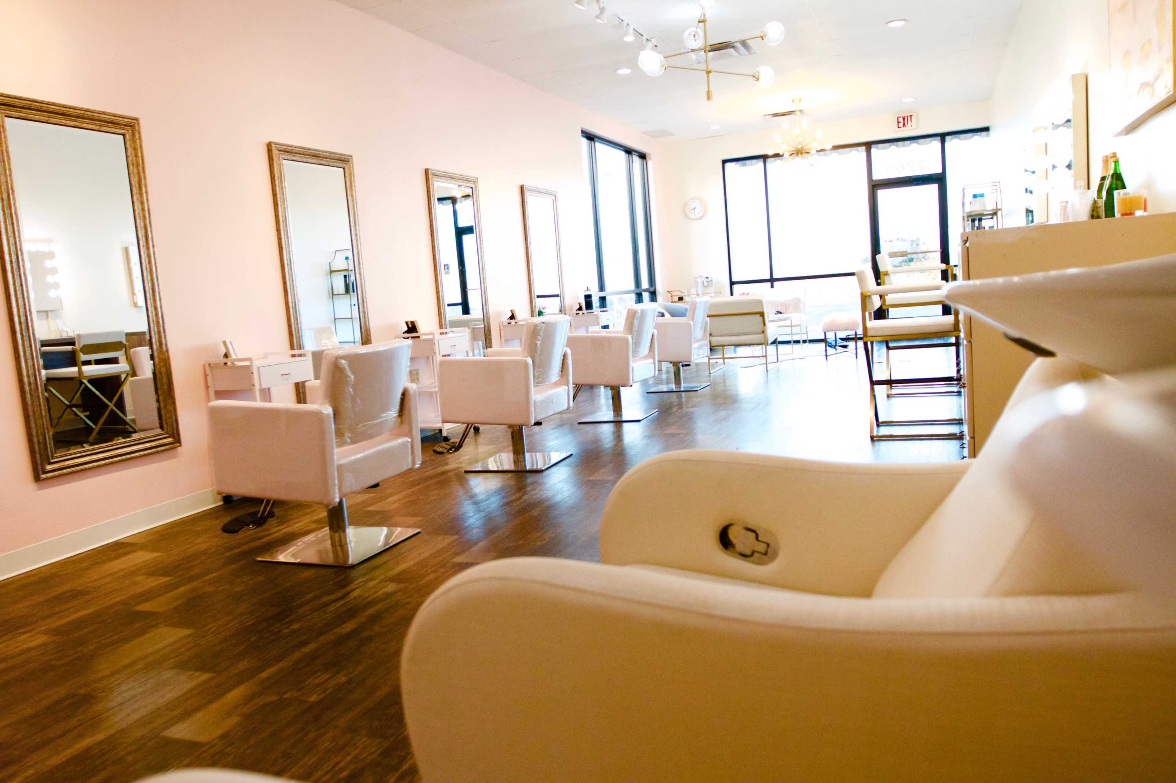 A modern hair salon with white chairs, large mirrors, and a bright, open space with natural light.