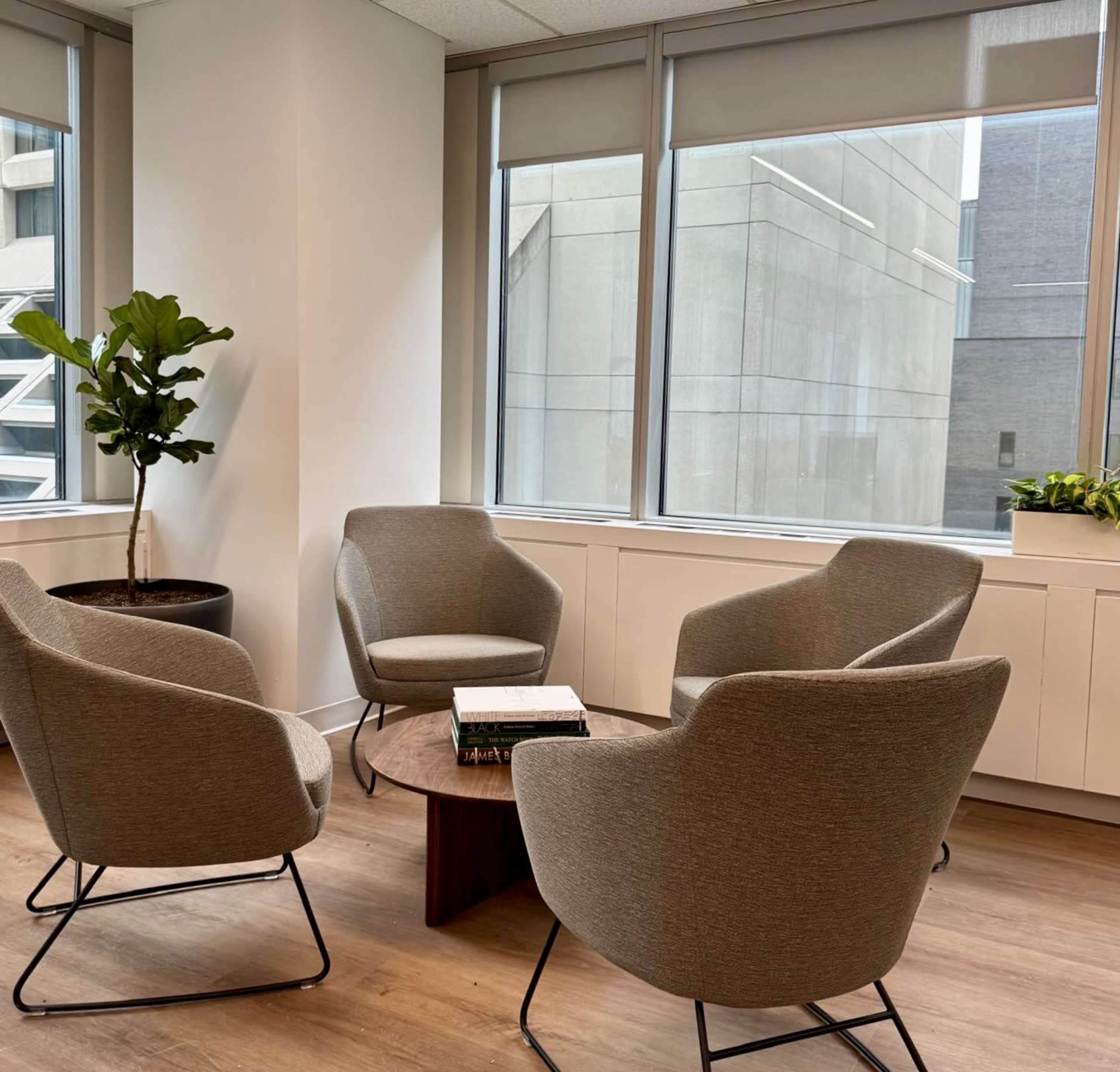 The image shows a modern office corner with four upholstered chairs arranged around a small table near large windows.