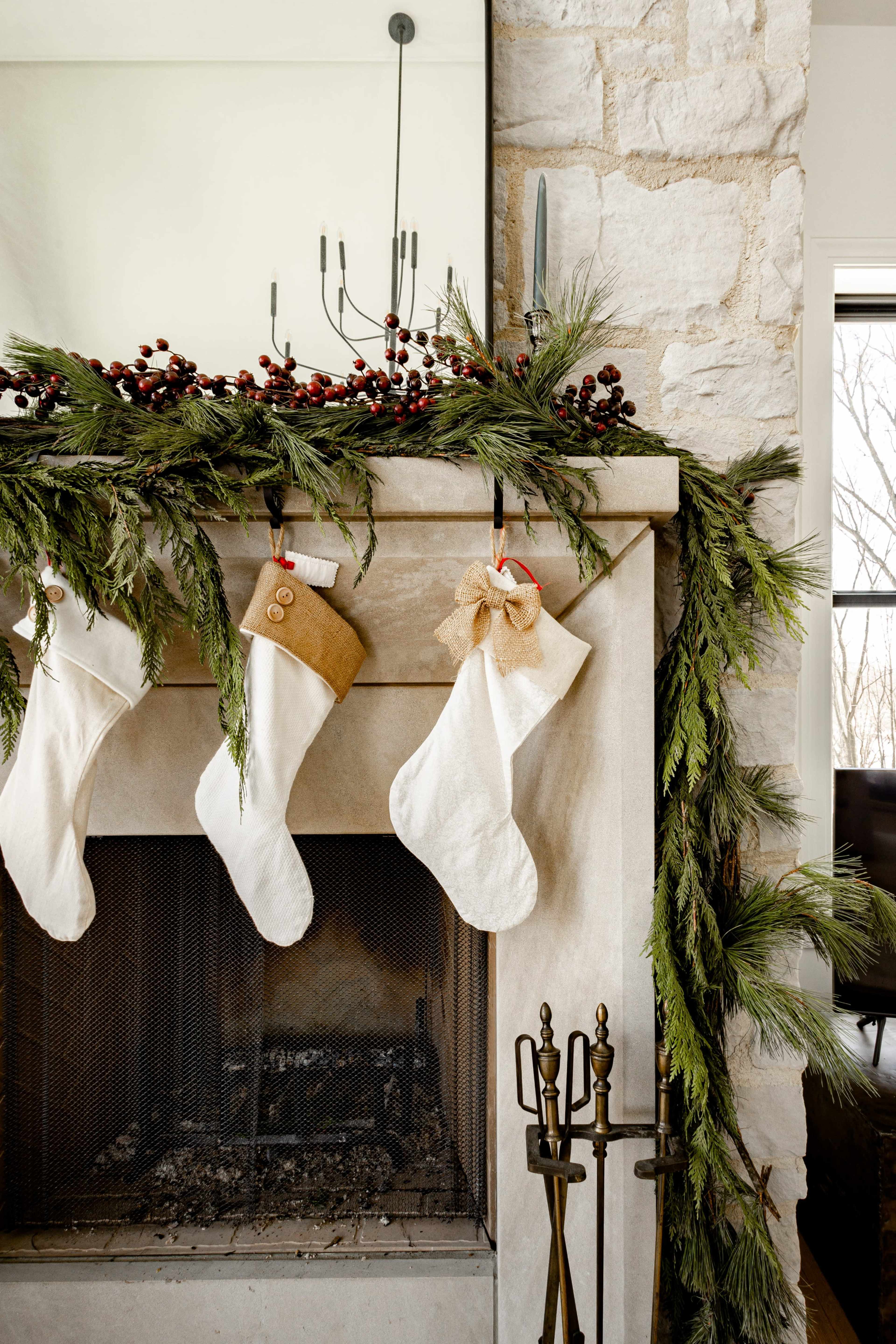 The image shows a decorated fireplace mantel adorned with evergreen garlands, red berries, and several white stockings hanging from it.