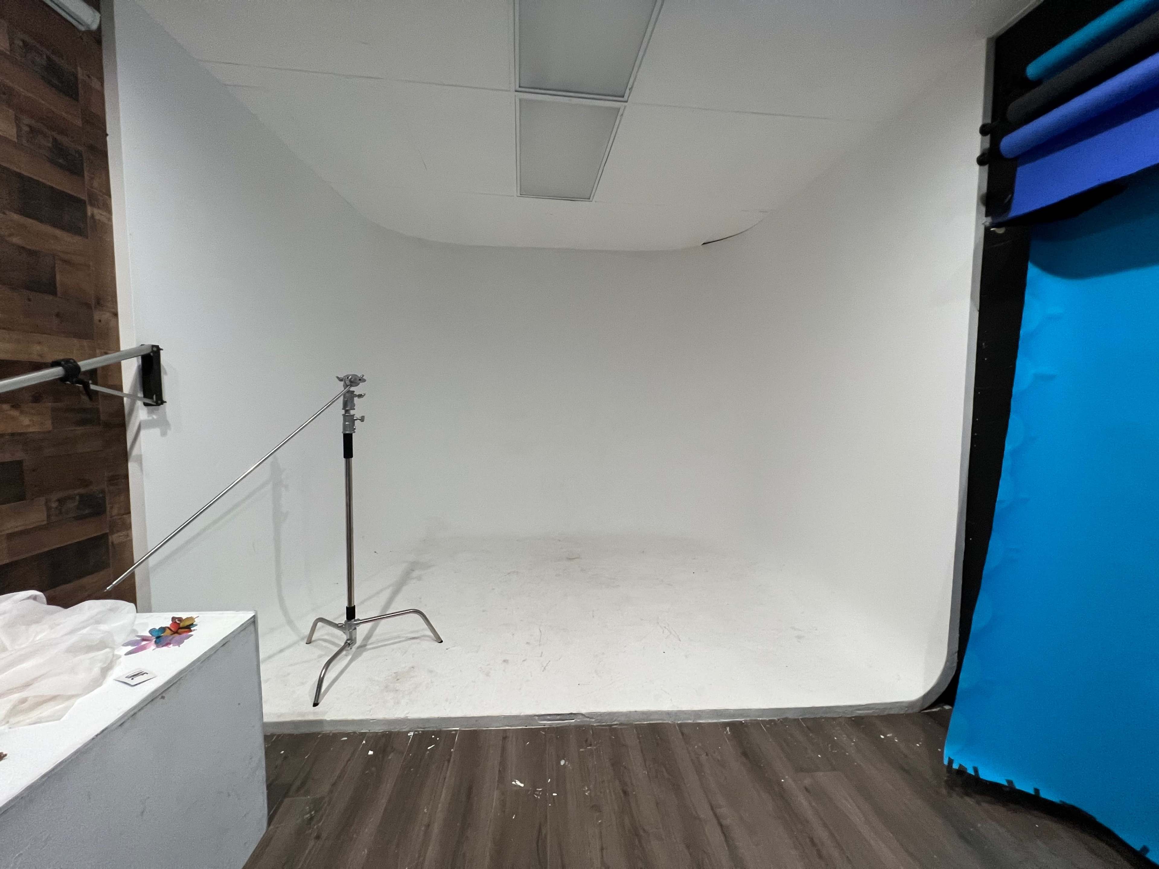 A minimalist photo studio with a white curved wall, a metal stand, and a blue backdrop area.