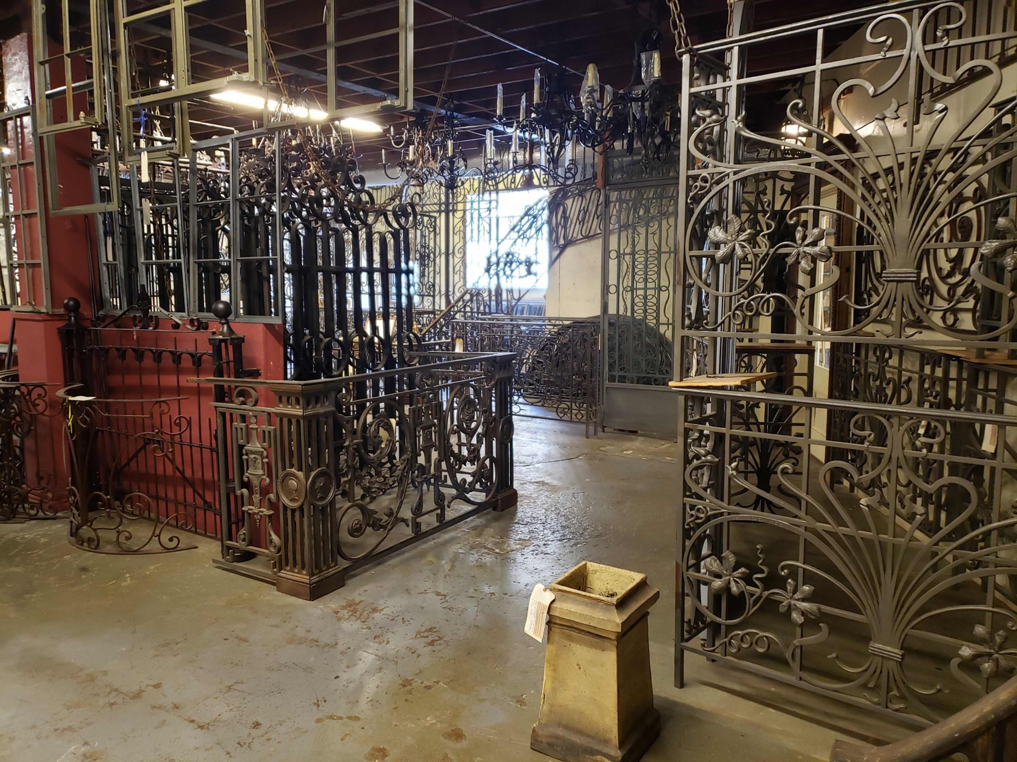 The image shows a workshop or storage area filled with various decorative iron gates and fences arranged in a large space.