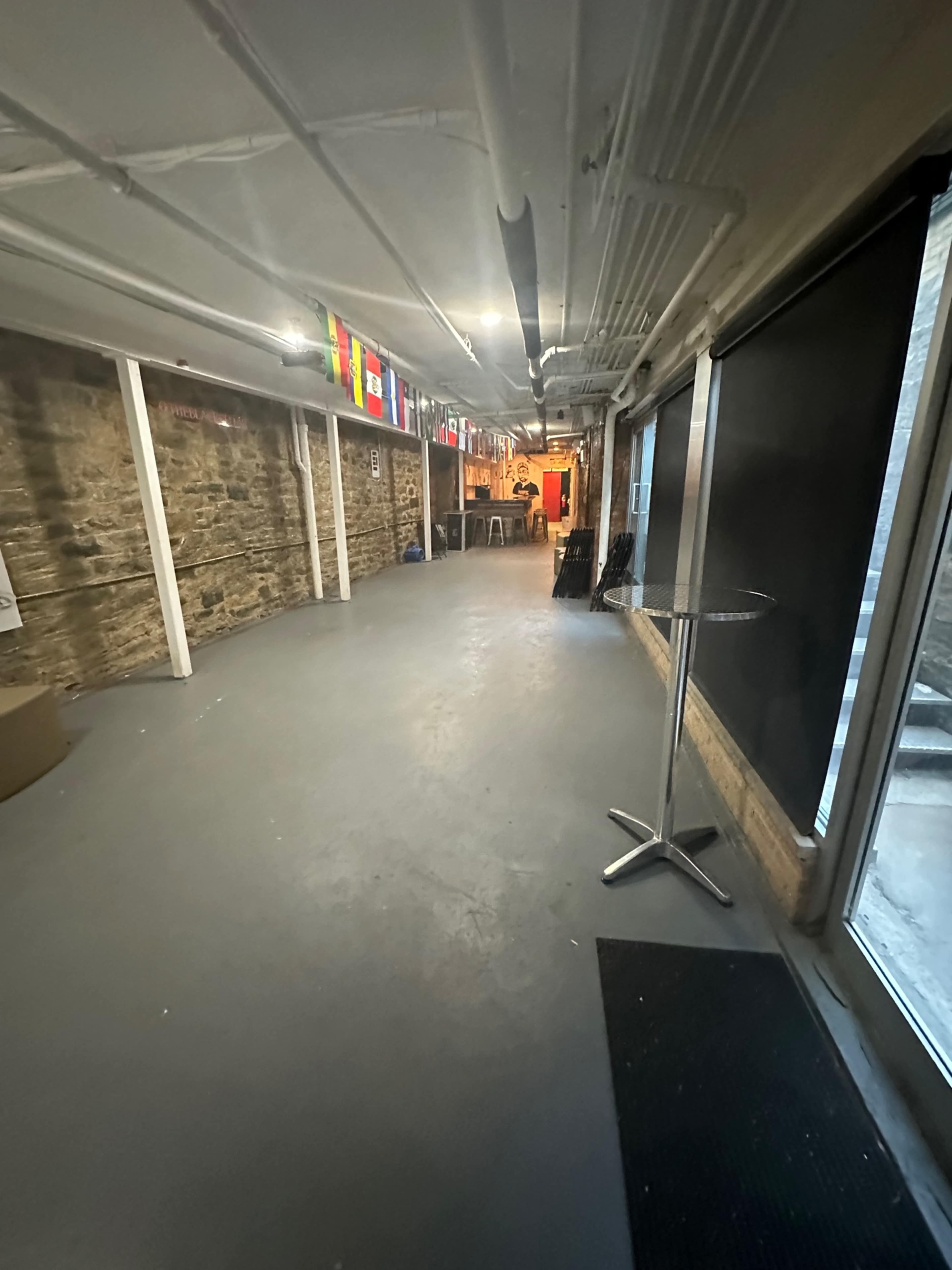 The image shows a long hallway with stone walls, gray flooring, a table, and flags hanging from the ceiling.