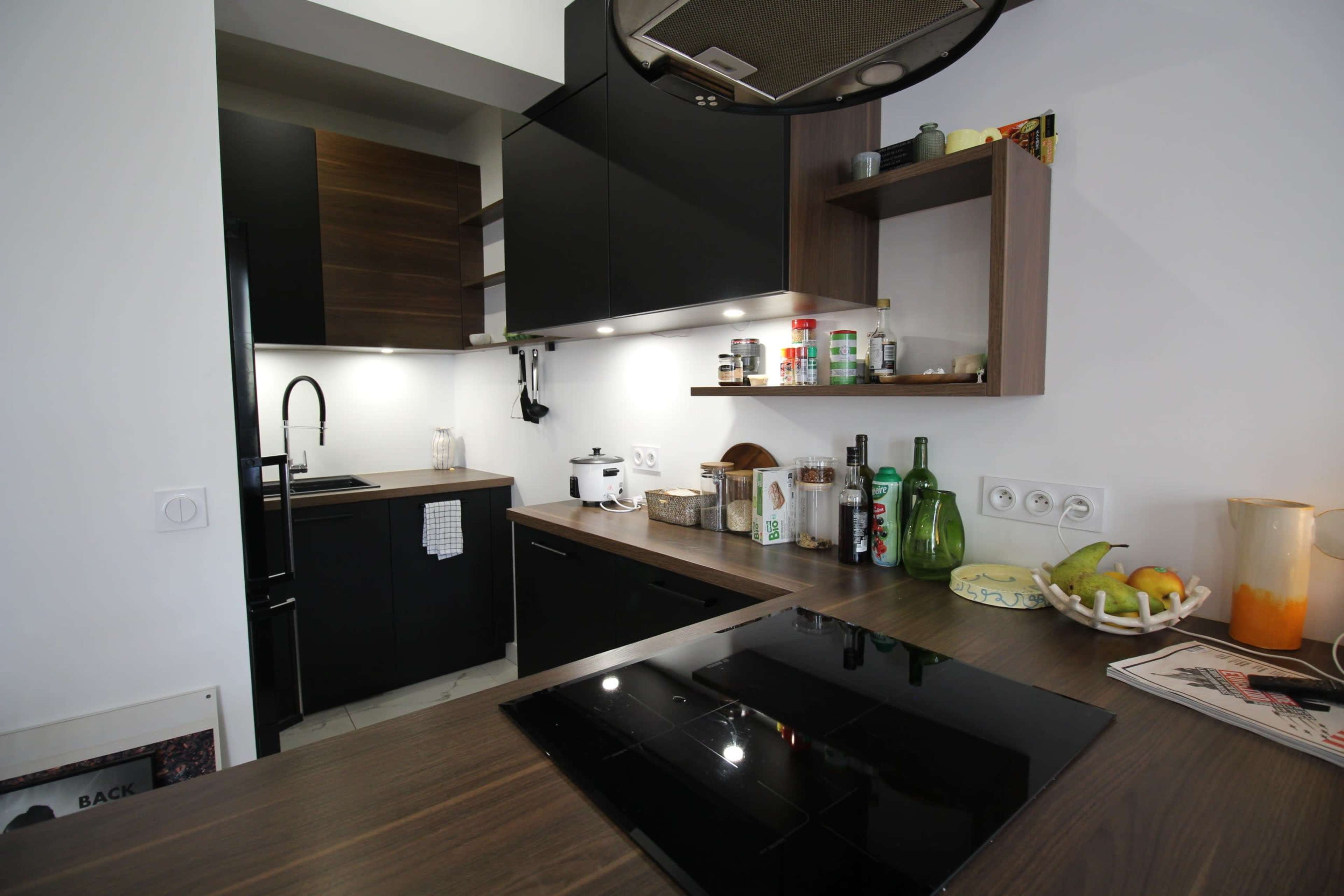 The image shows a modern kitchen featuring dark cabinetry, a countertop with an induction cooktop, and various kitchen appliances and decor on display.