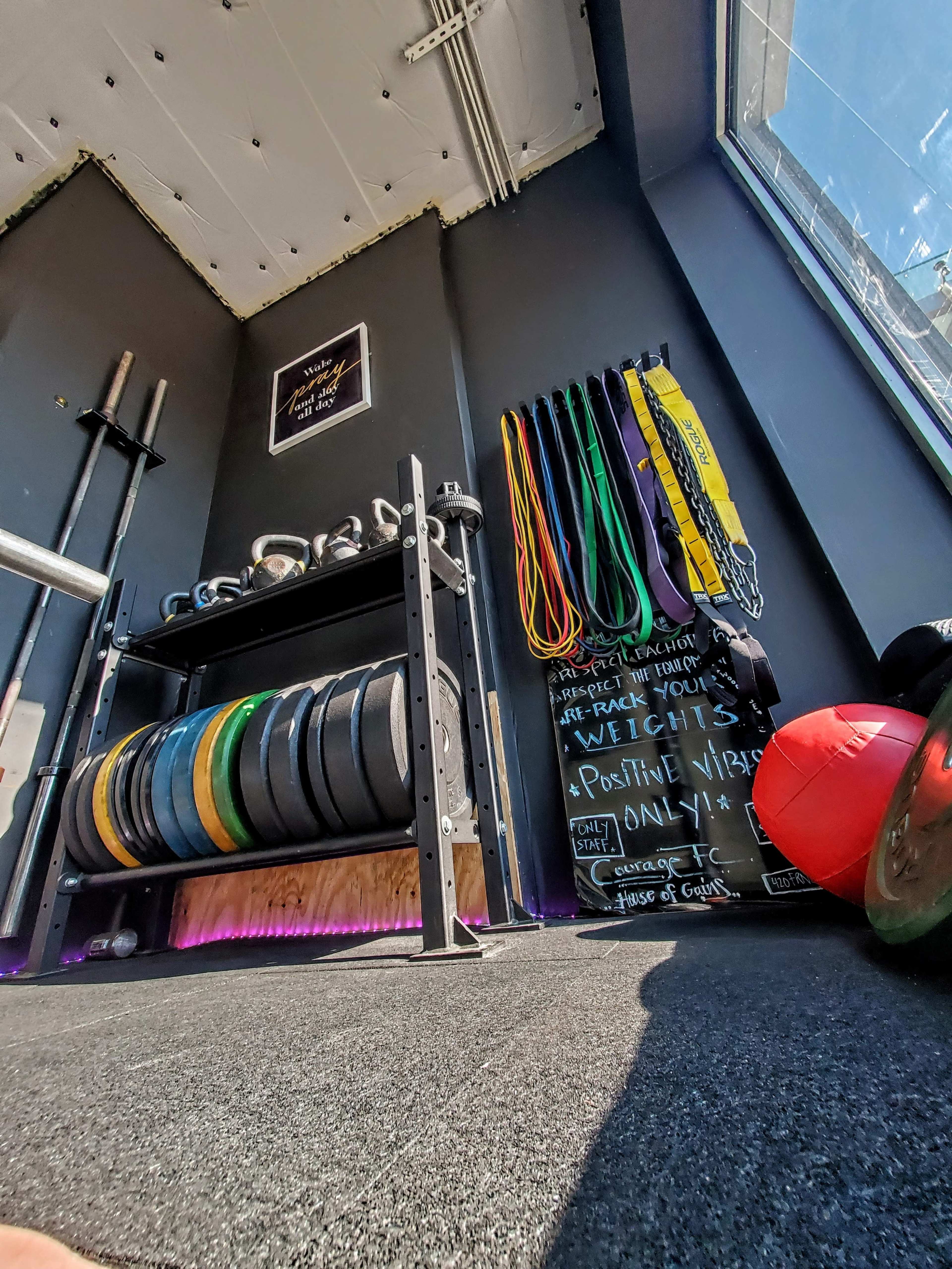 A well-organized gym corner displays weight plates on a rack, resistance bands hanging on the wall, and motivational quotes written on a chalkboard.