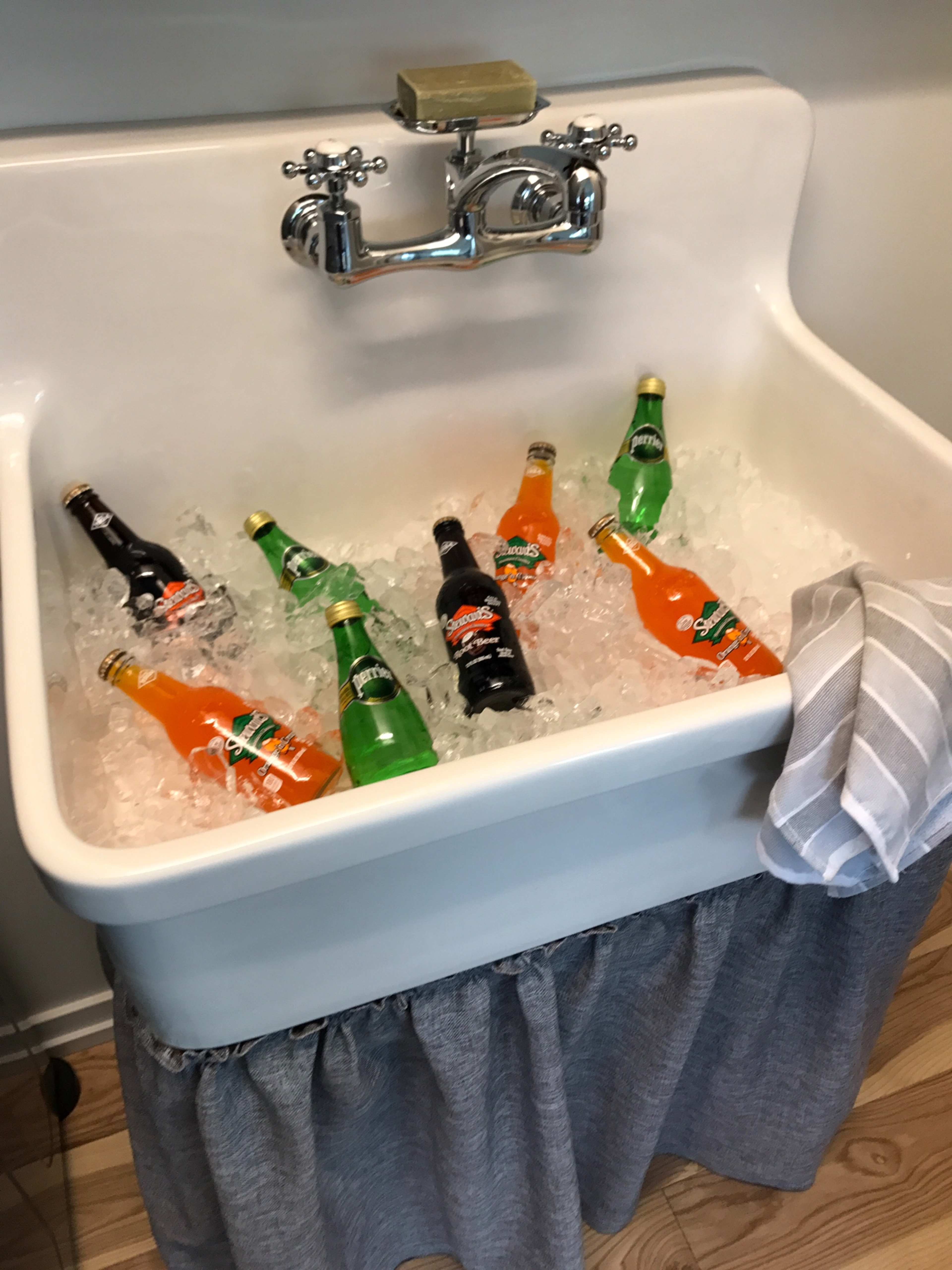 A vintage sink is filled with ice and various colored glass soda bottles.