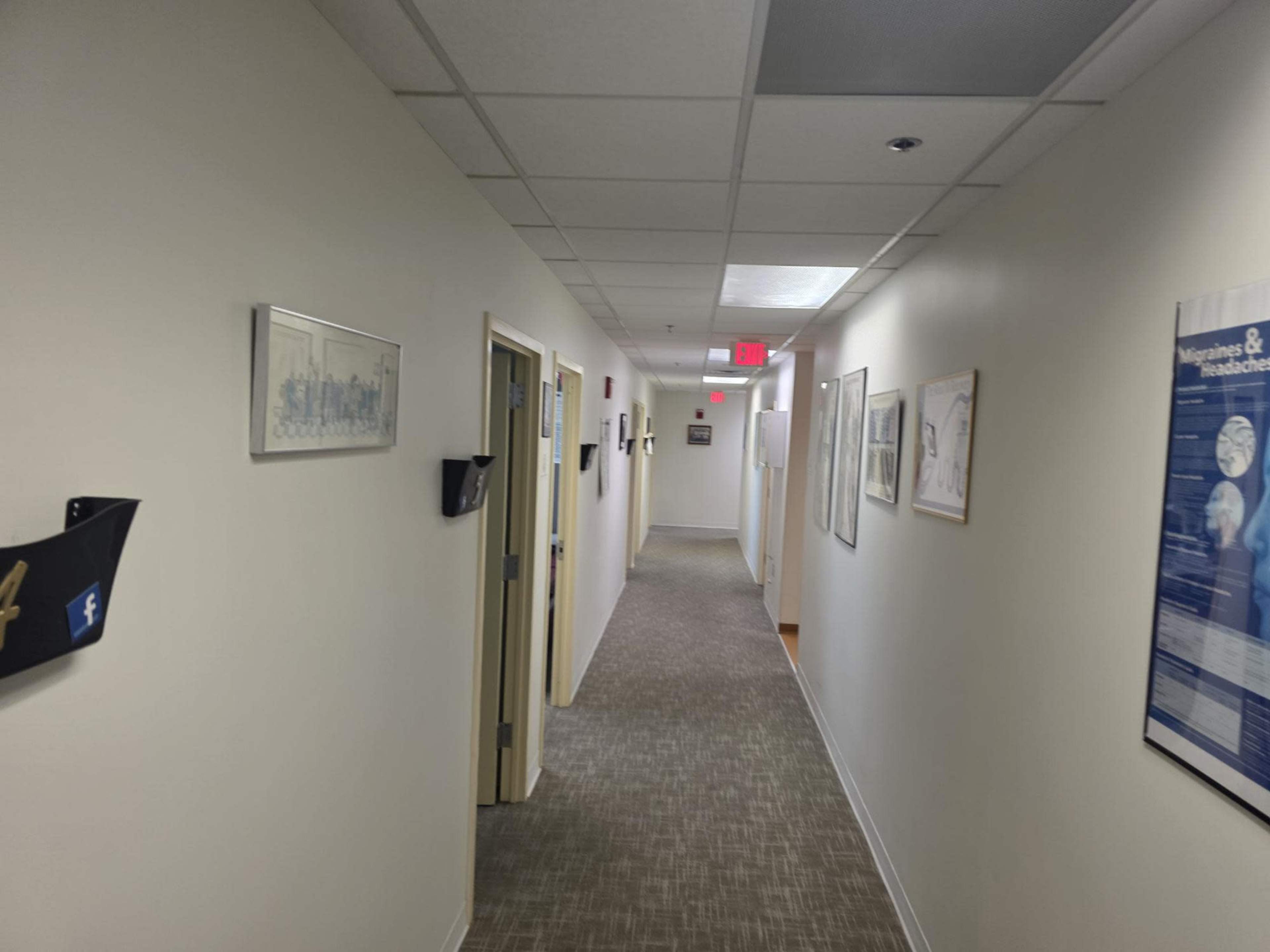 A hallway is lined with framed pictures and doors leading to offices, with overhead lights illuminating the space.