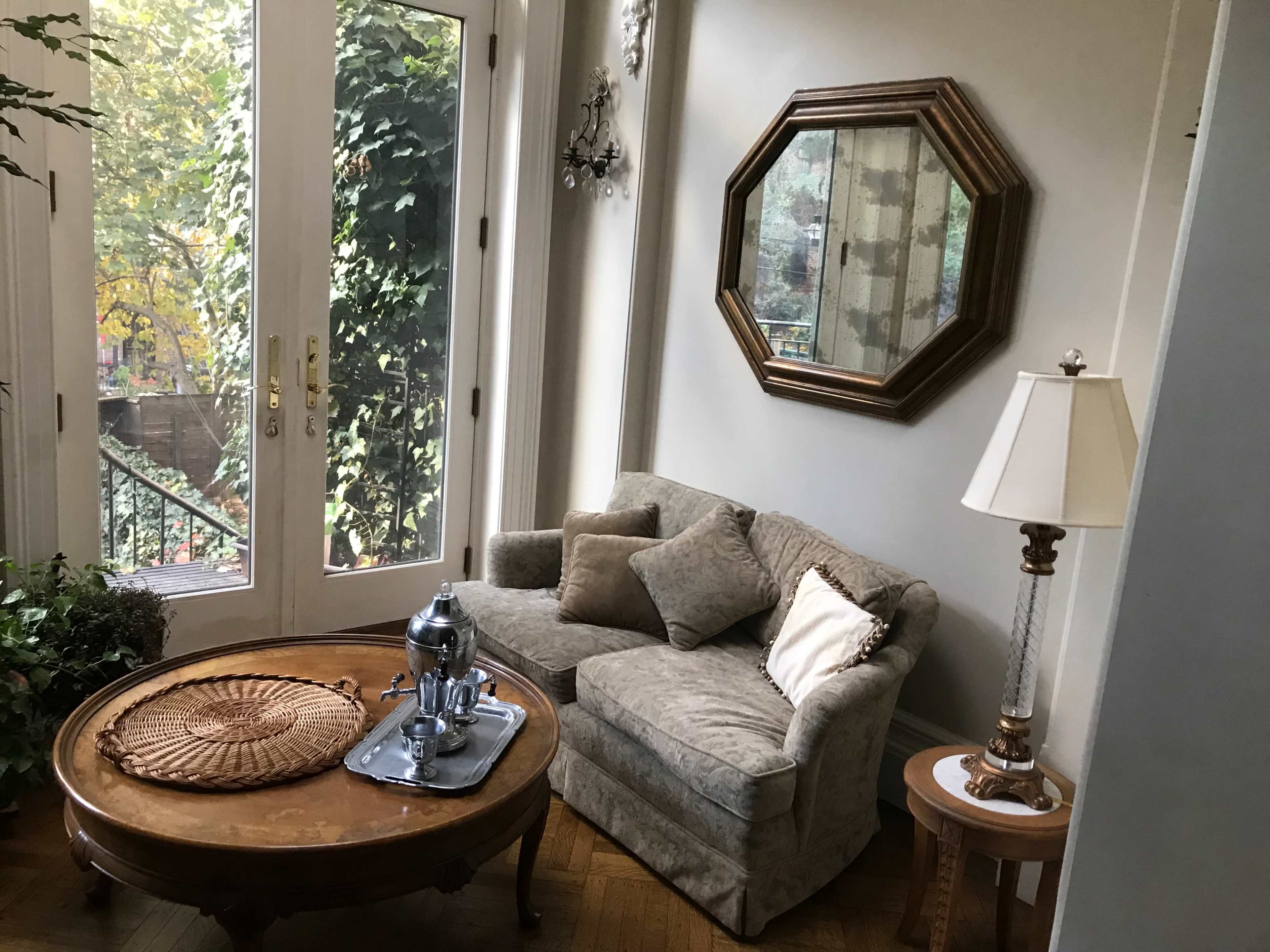 A small living area with a sofa, a wooden coffee table with a tray, a lamp, and large windows overlooking greenery.