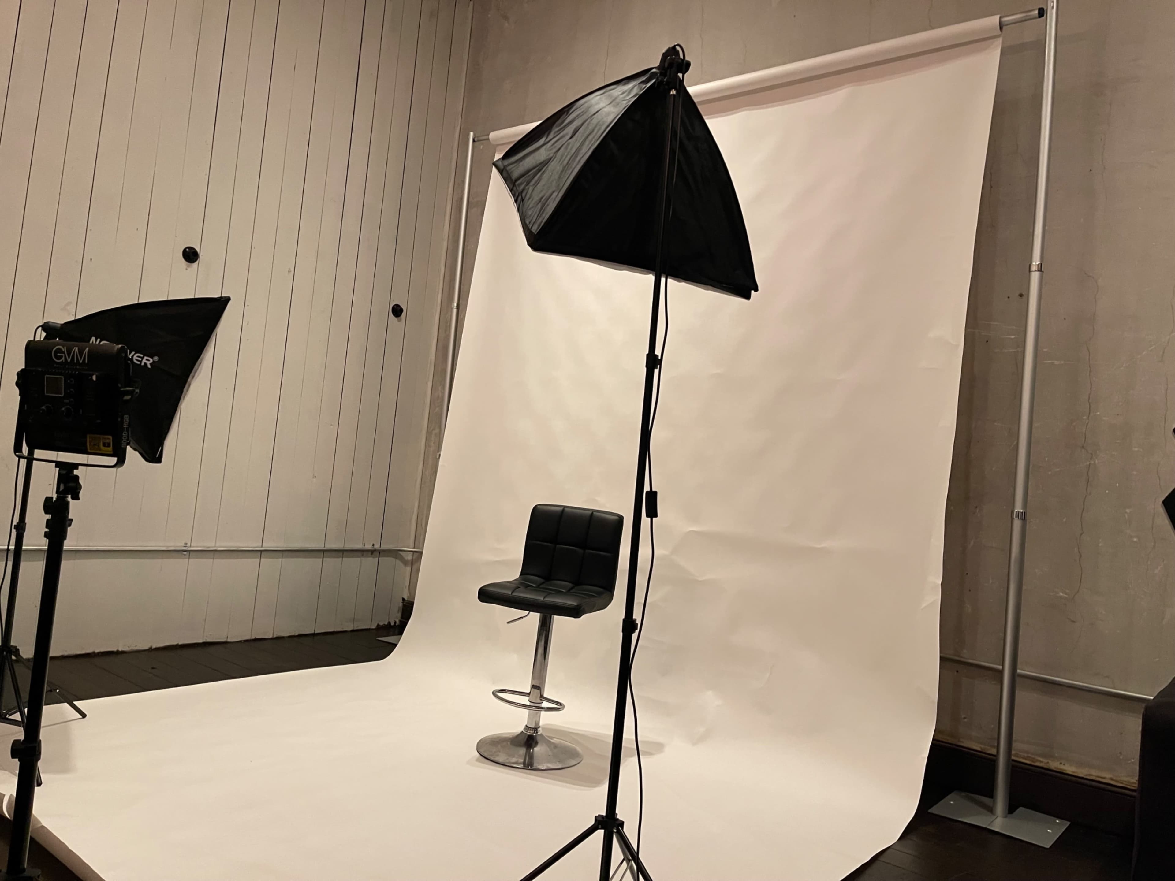 A black swivel chair is positioned on a white backdrop in a photography studio, illuminated by softbox lights.