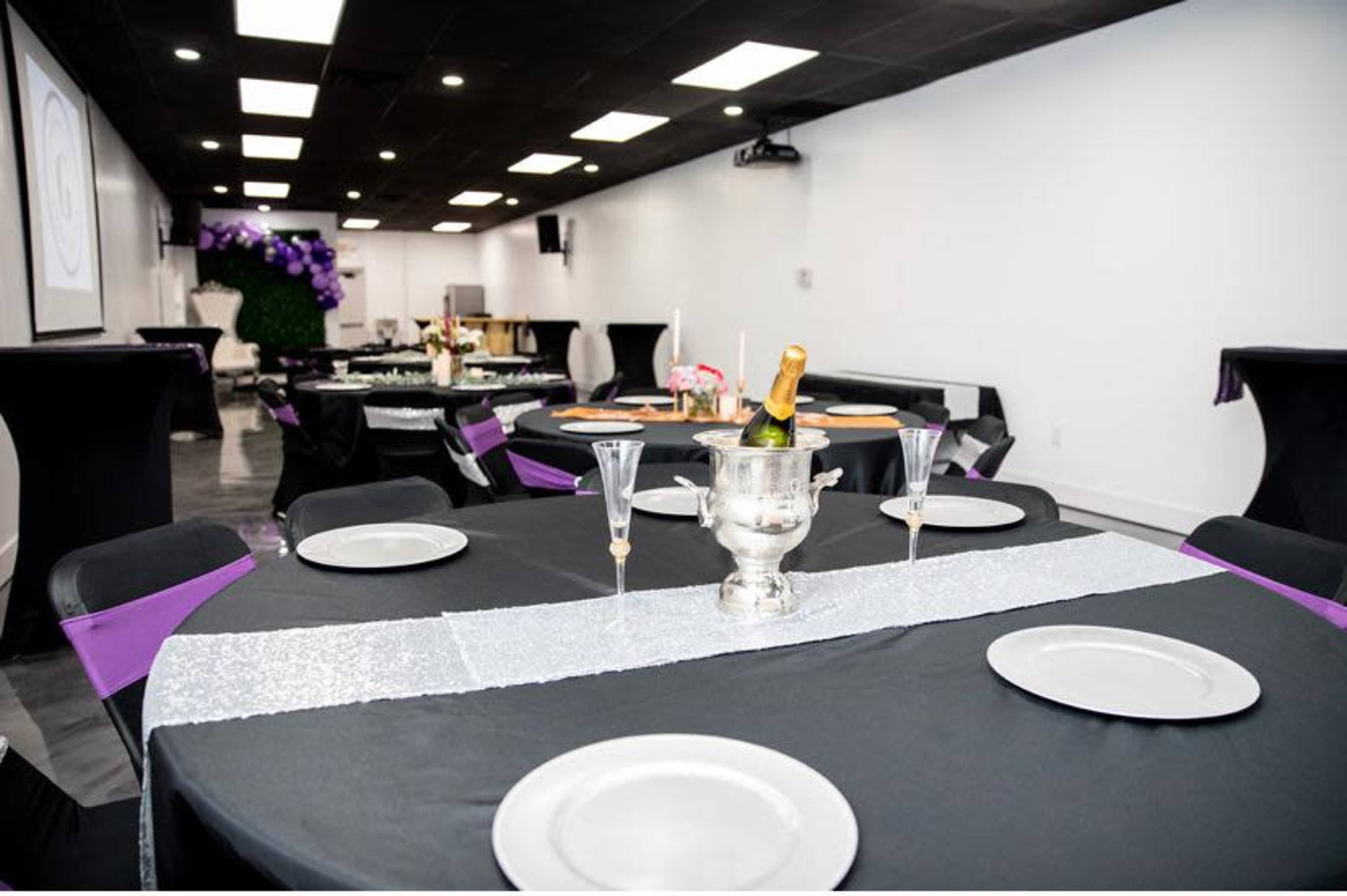 A banquet hall set up with black tables adorned with purple accents, featuring plates and sparkling wine in silver ice buckets.