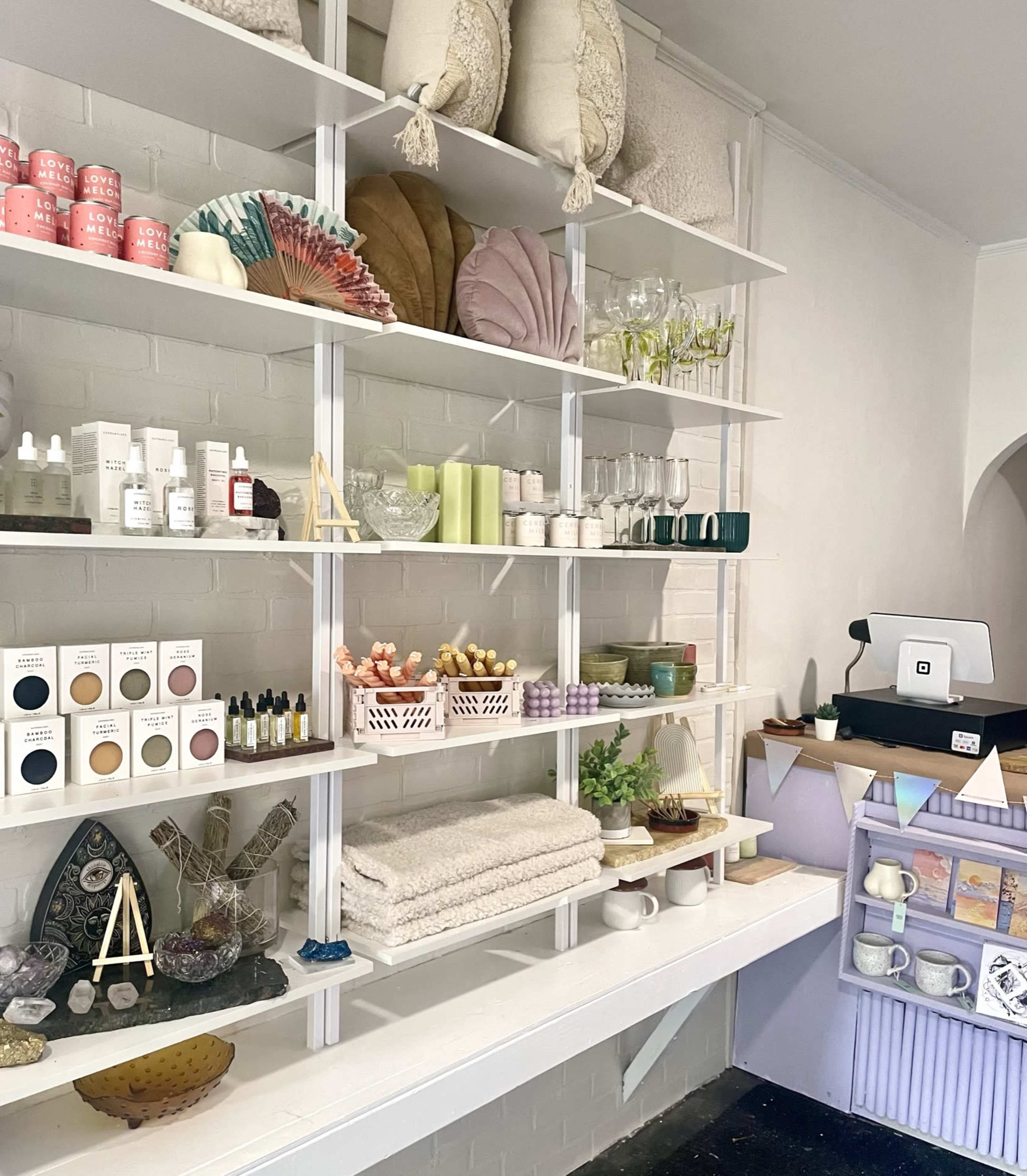A neatly organized display of home decor items, skincare products, and household essentials is arranged on white shelves against a light-colored wall.