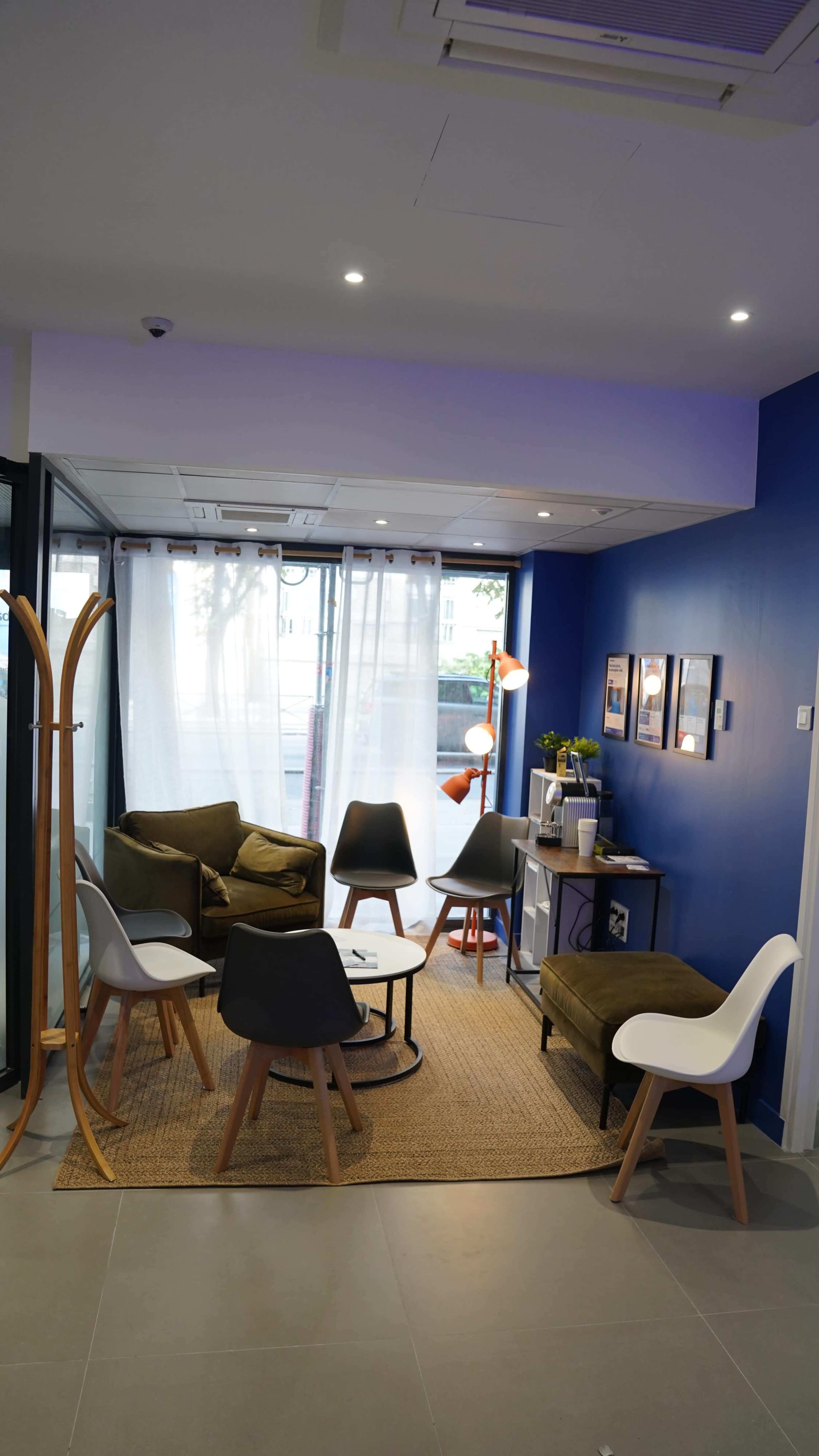 The image shows a modern lounge area featuring several chairs, a coffee table, and a decorative lamp against a blue wall.