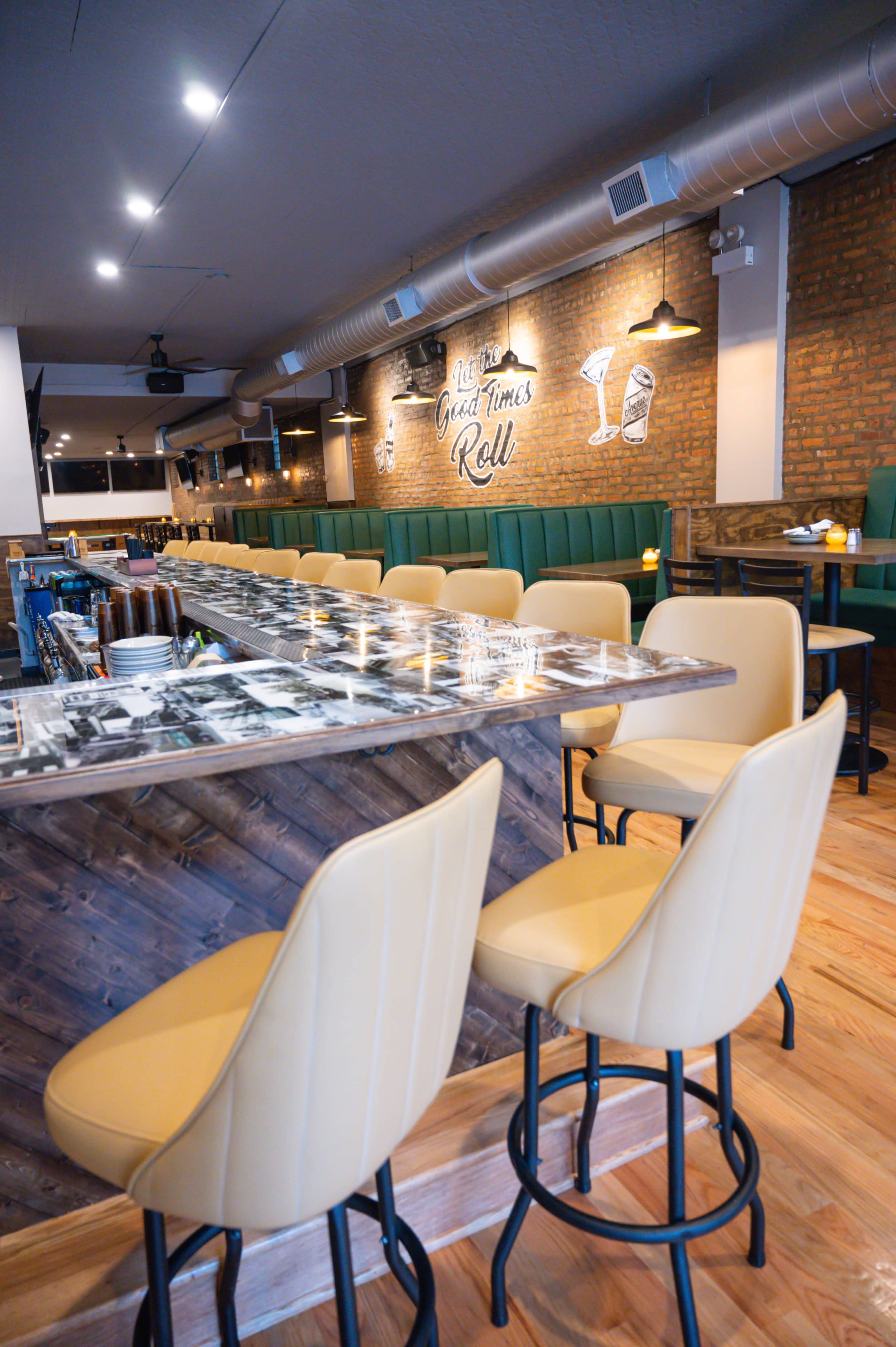 The image shows a modern bar with green seating and a long, metallic countertop, illuminated by soft lighting.