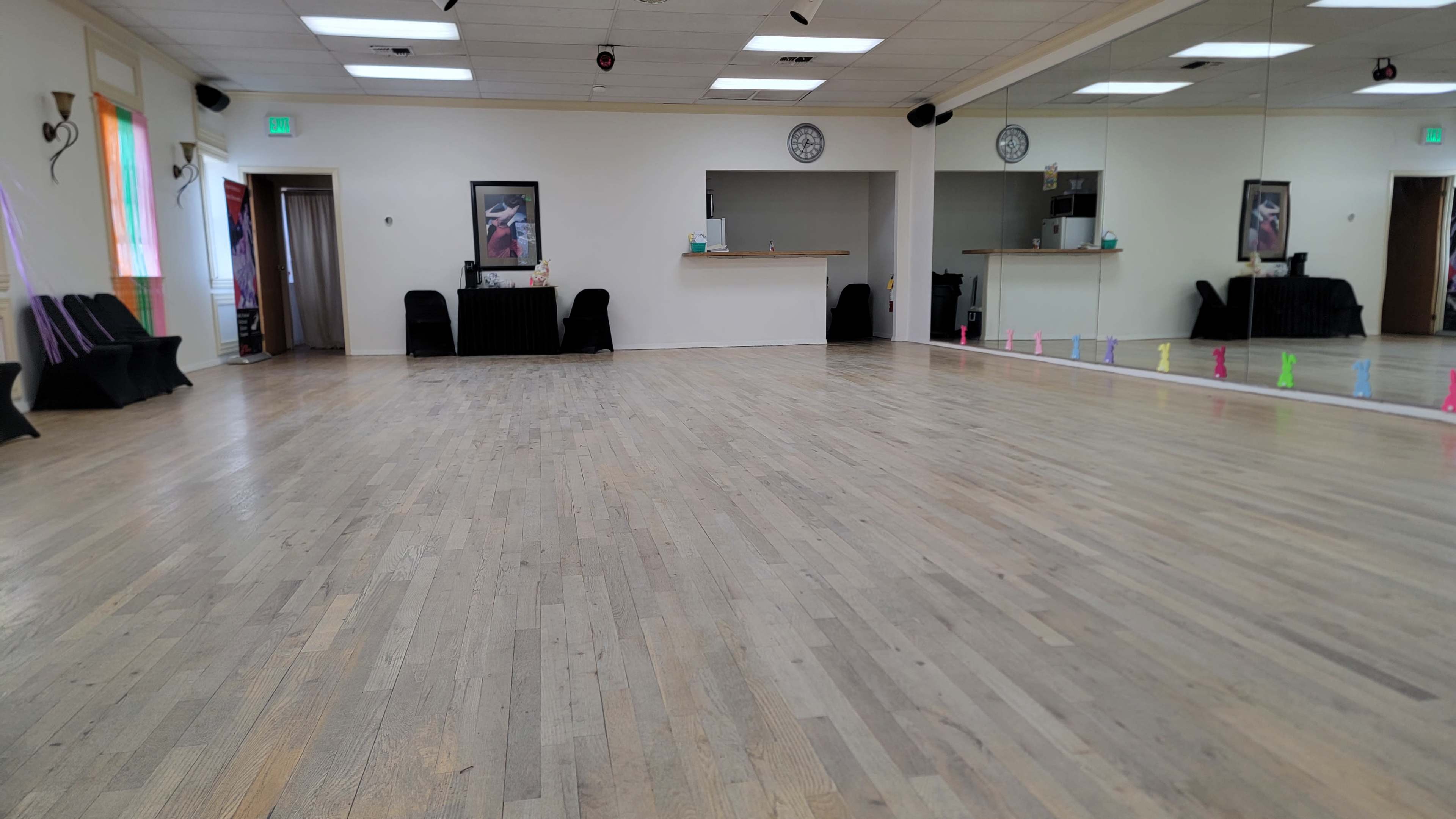 The image shows a spacious dance studio with wooden floors, mirrors on one wall, and seating along the sides.