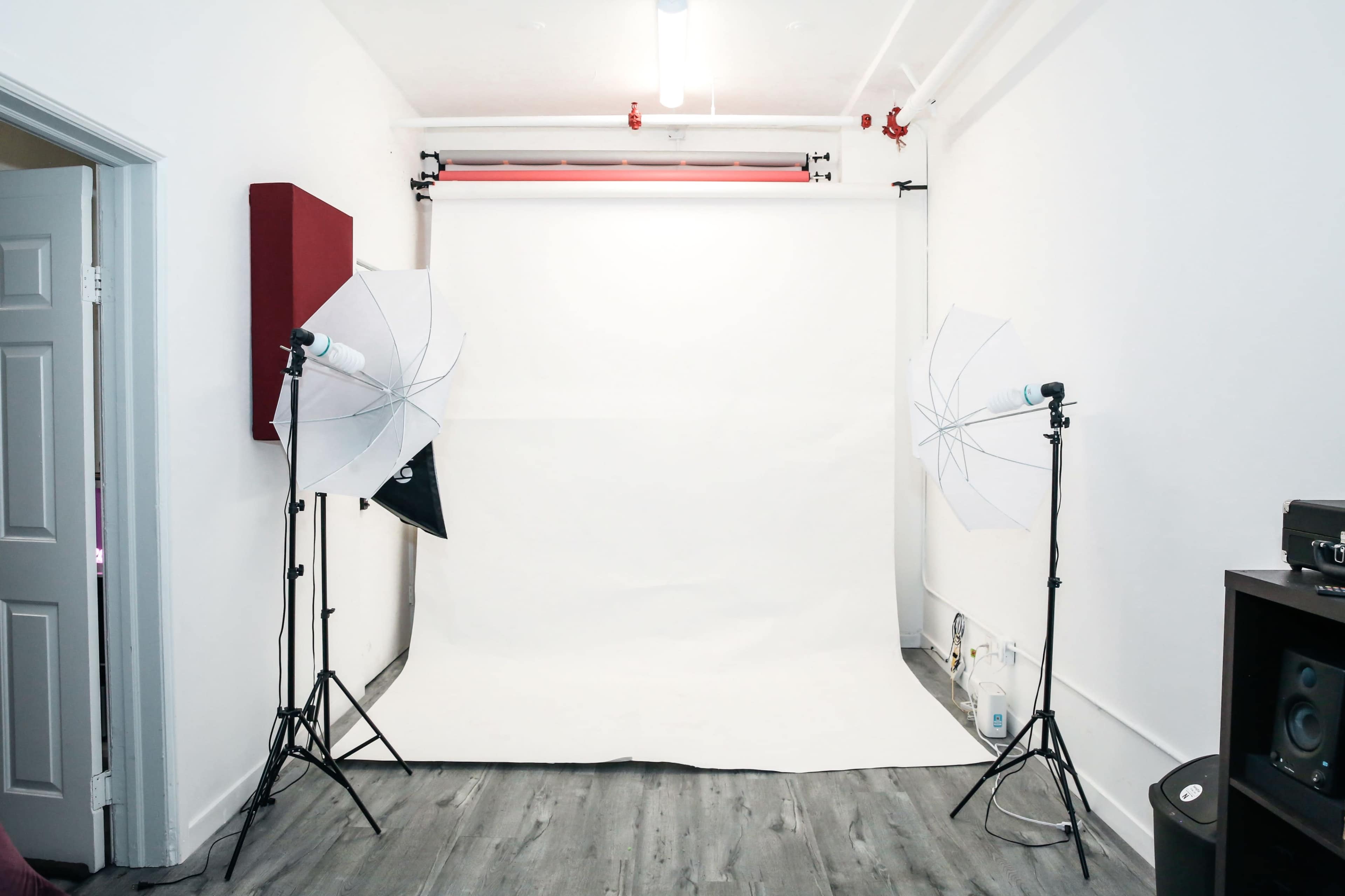 The image shows a photography studio with a plain white backdrop and two softbox lights positioned on either side.