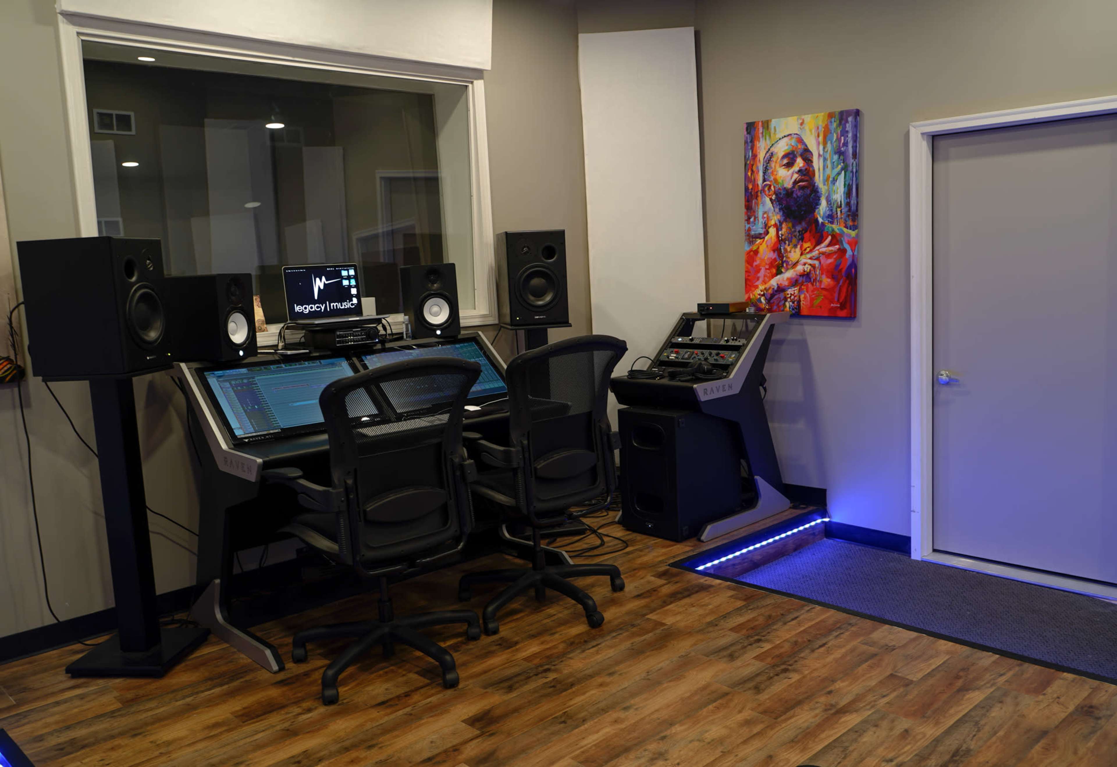 A music production studio featuring a digital audio workstation, two large speakers, and a colorful artwork on the wall.