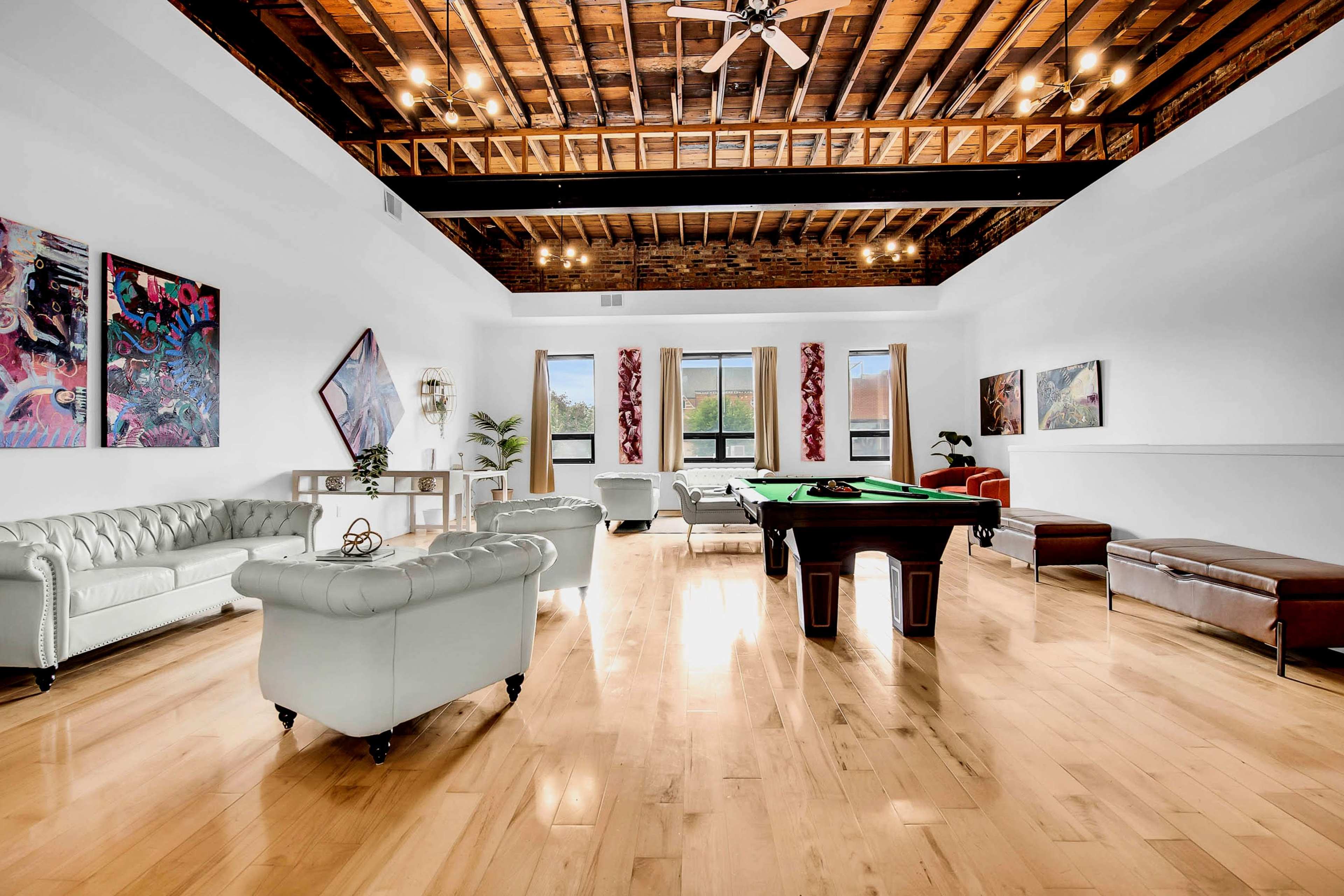 A spacious room with a wooden ceiling, featuring a pool table, leather seating, and colorful wall art.