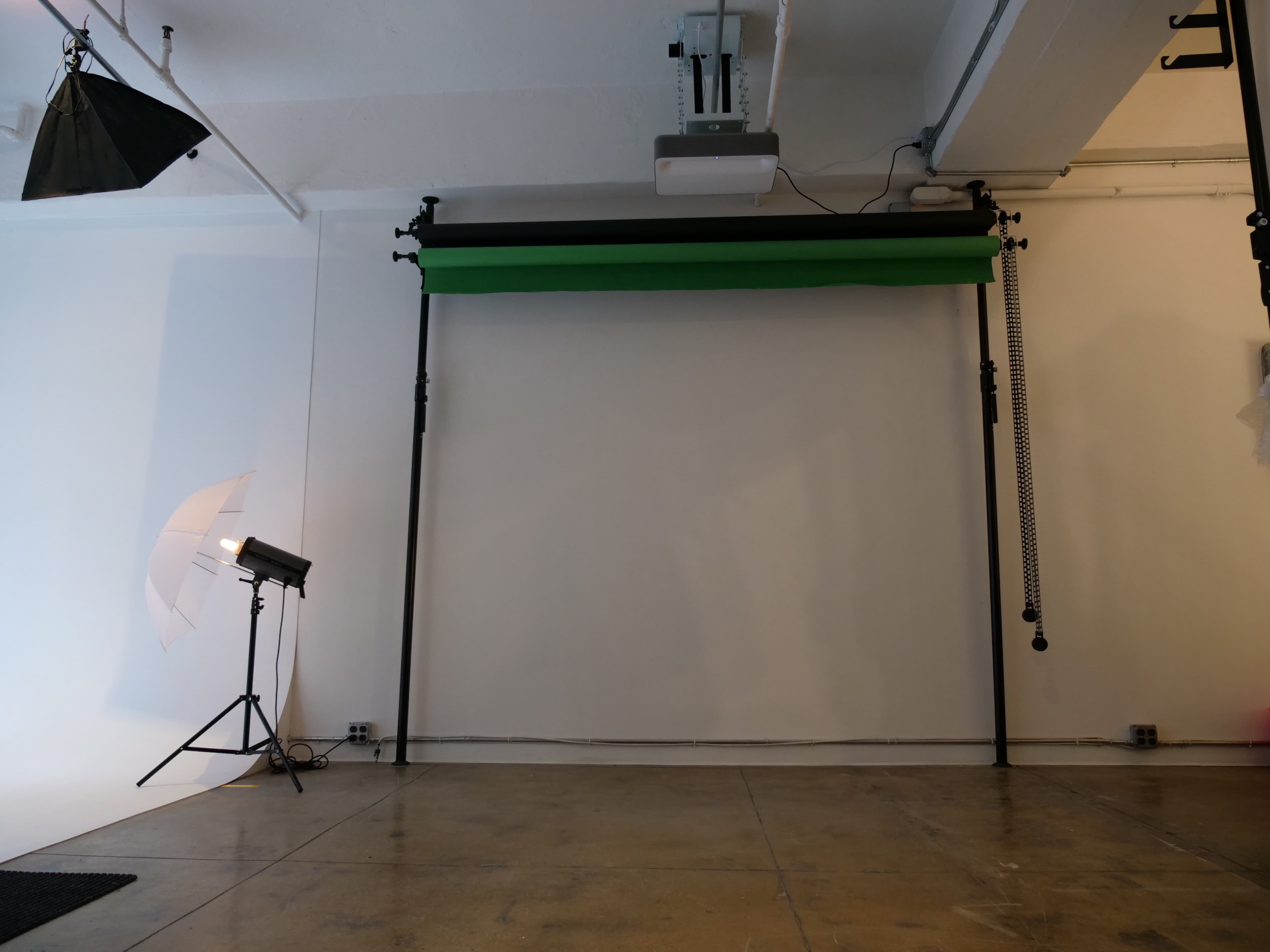 A photography studio with a green backdrop, lighting equipment, and a plain white wall.