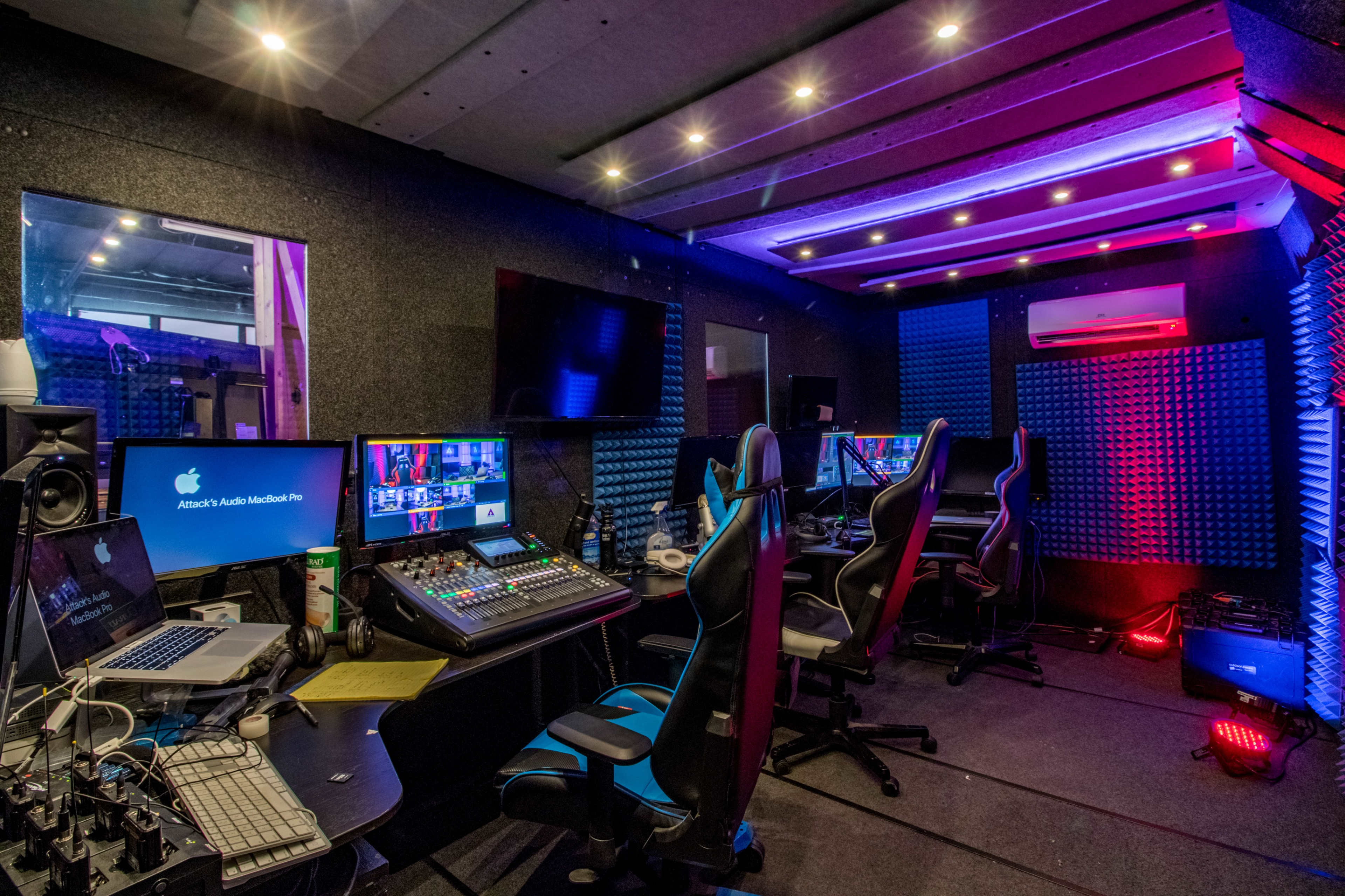 A modern recording studio with multiple computer workstations, audio equipment, and soundproofing panels.