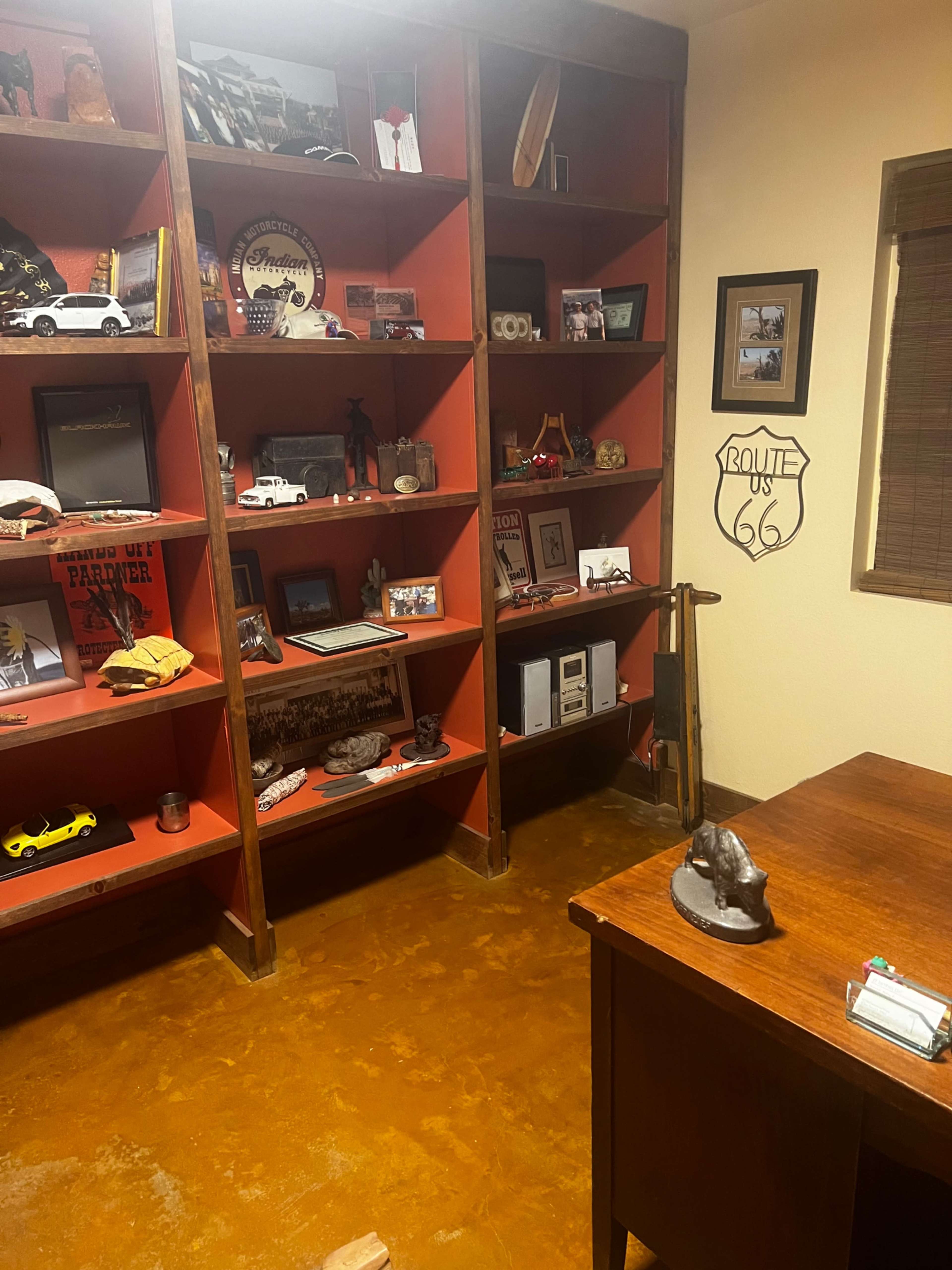 The image shows a home office with wooden shelves displaying various collectibles and a desk in the foreground.
