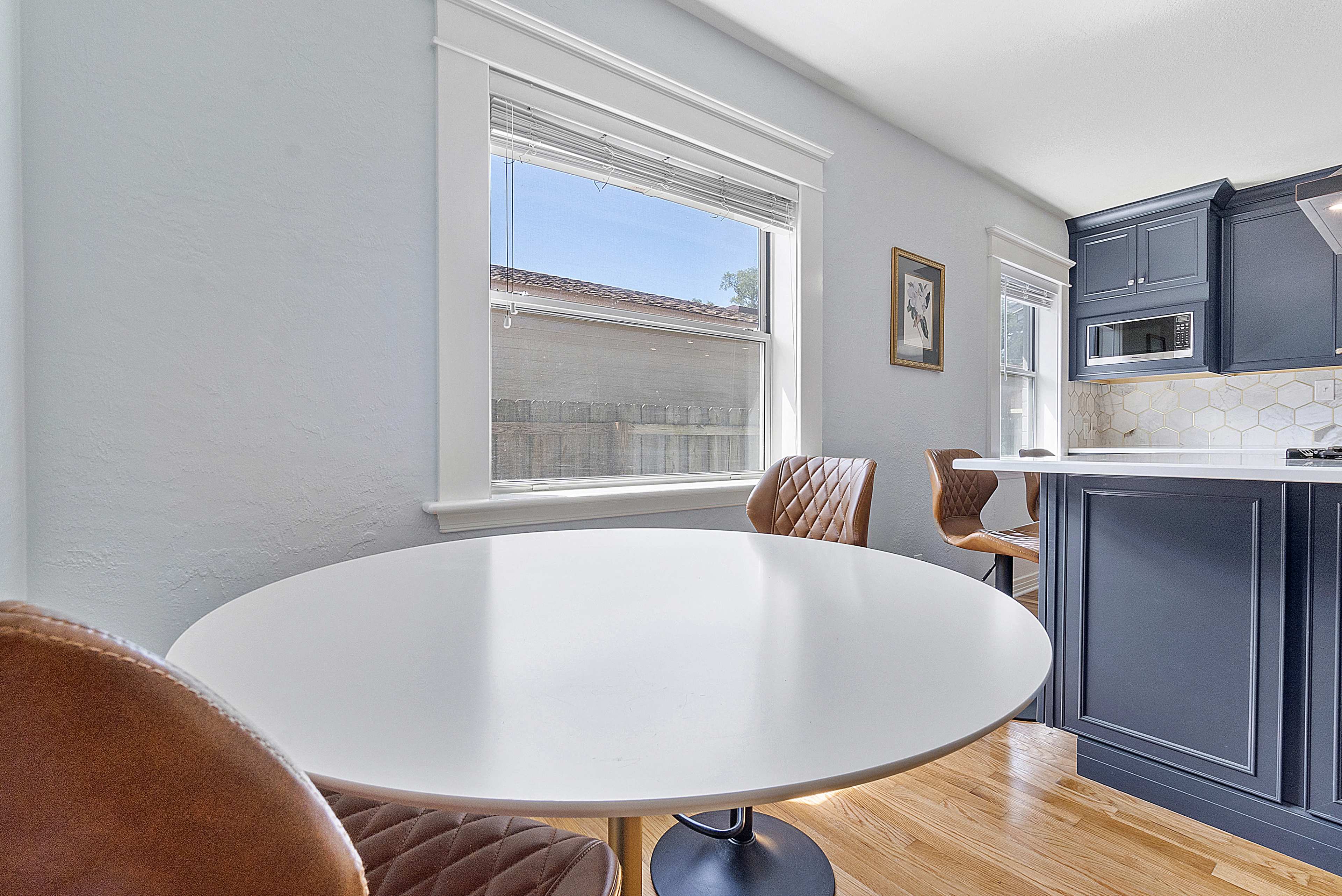 A round white dining table is positioned near a window in a kitchen with navy blue cabinets.