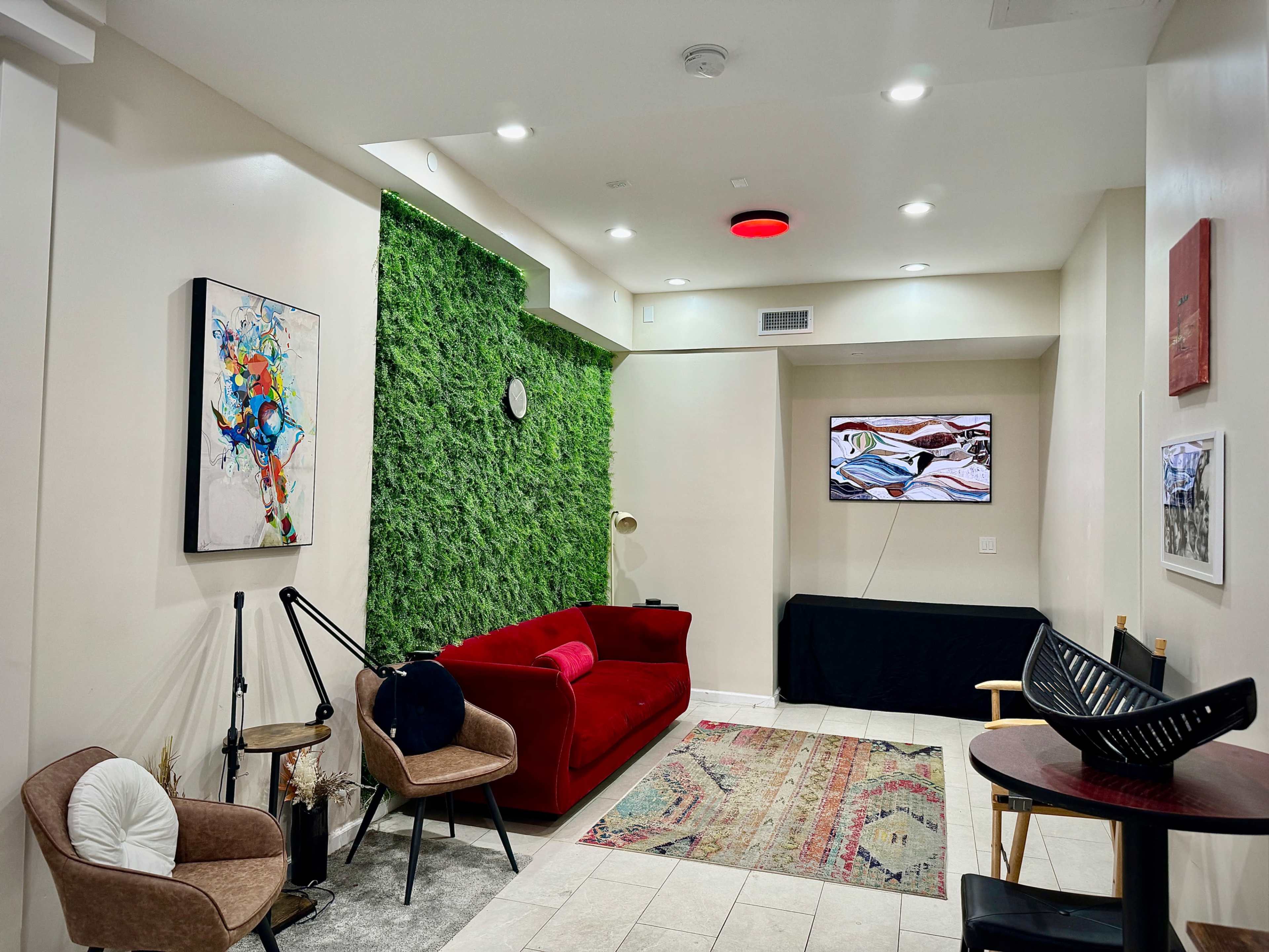 The image shows a contemporary living space featuring a red couch, two chairs, a textured green wall, a television, and various decorative items.