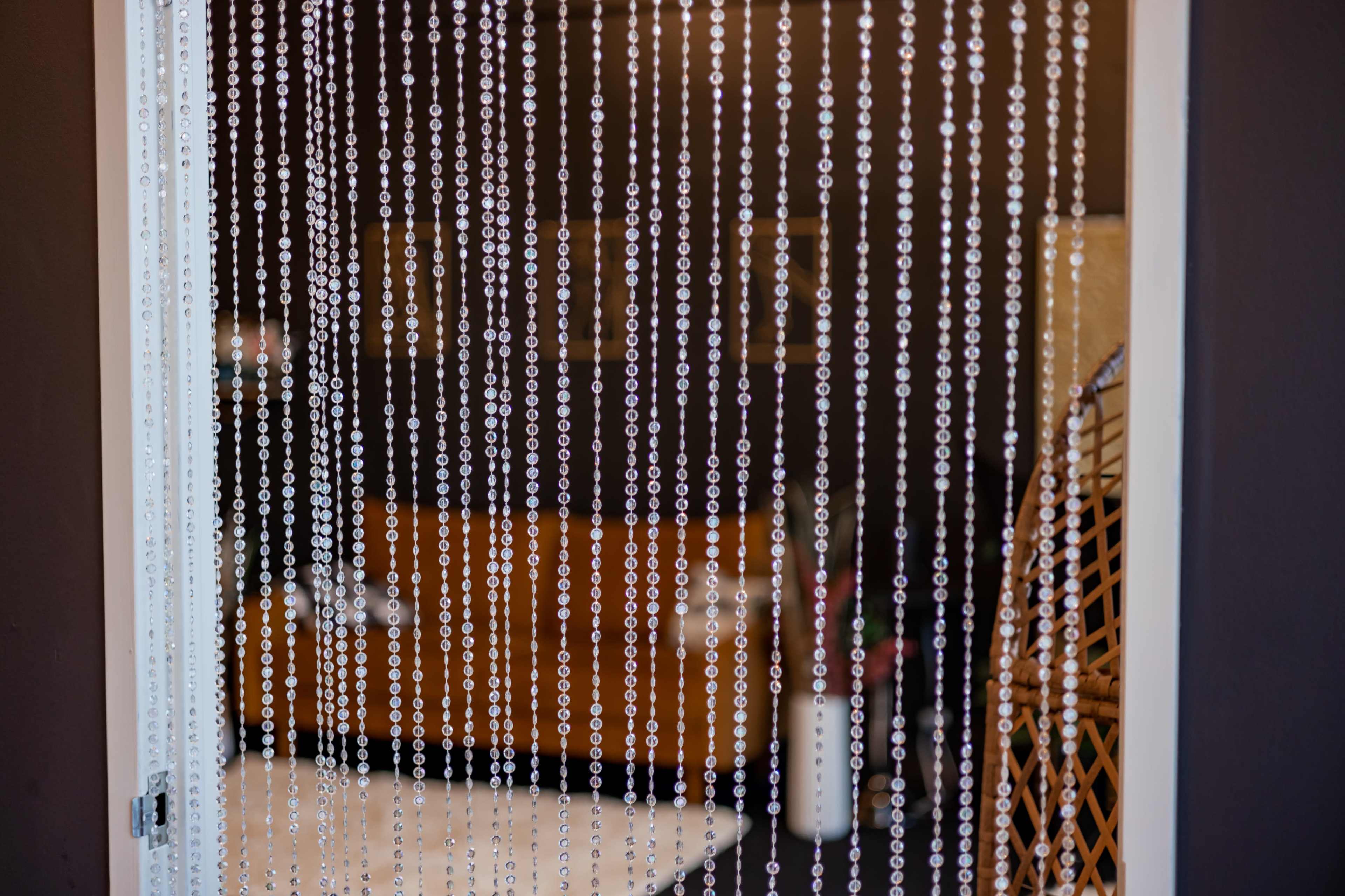 A curtain of beads hanging in front of a blurred interior space with a wooden couch and decorative elements.