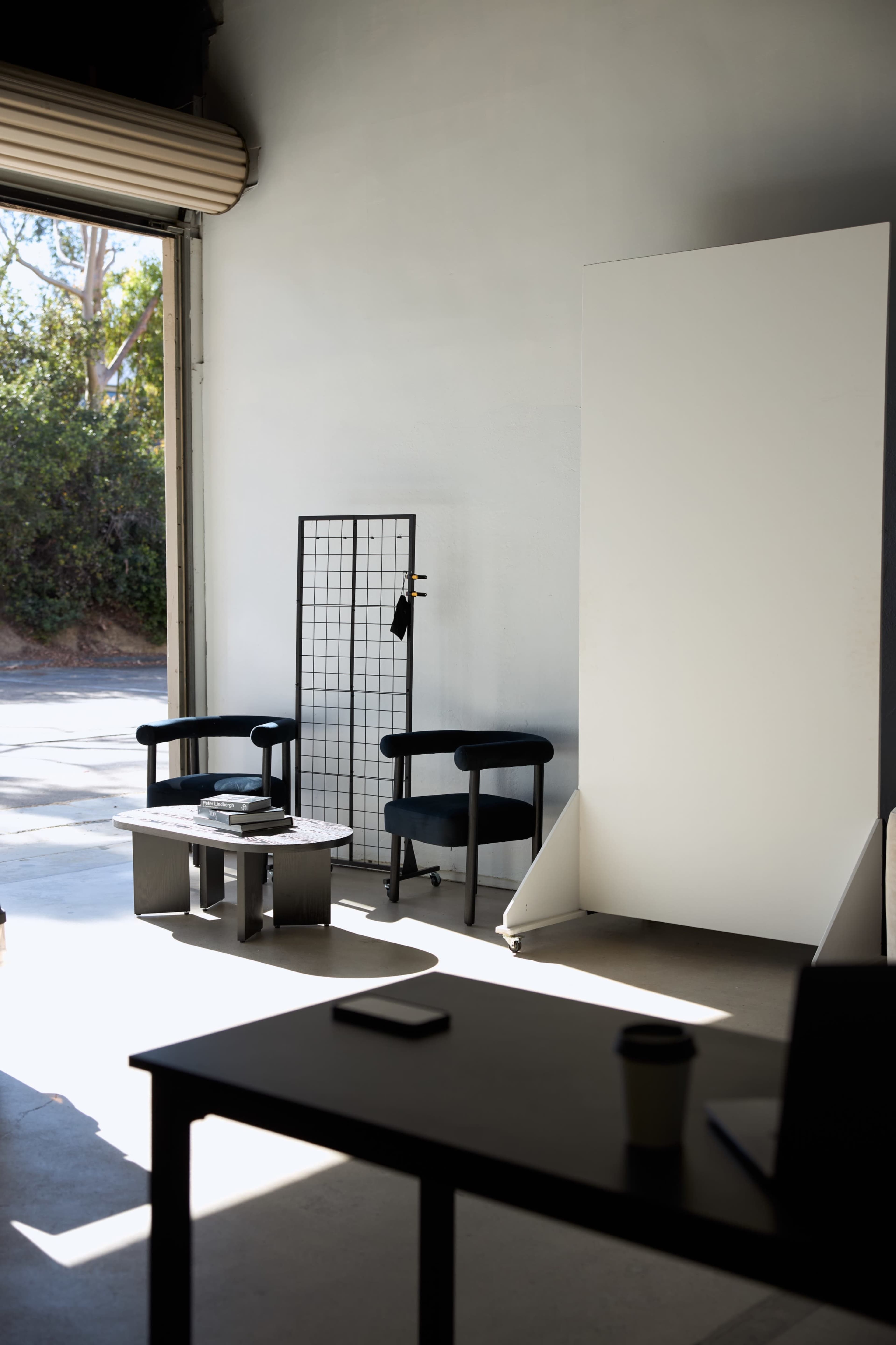 A small, modern interior features two chairs and a coffee table, with a grid panel and a large white backdrop in a well-lit space.