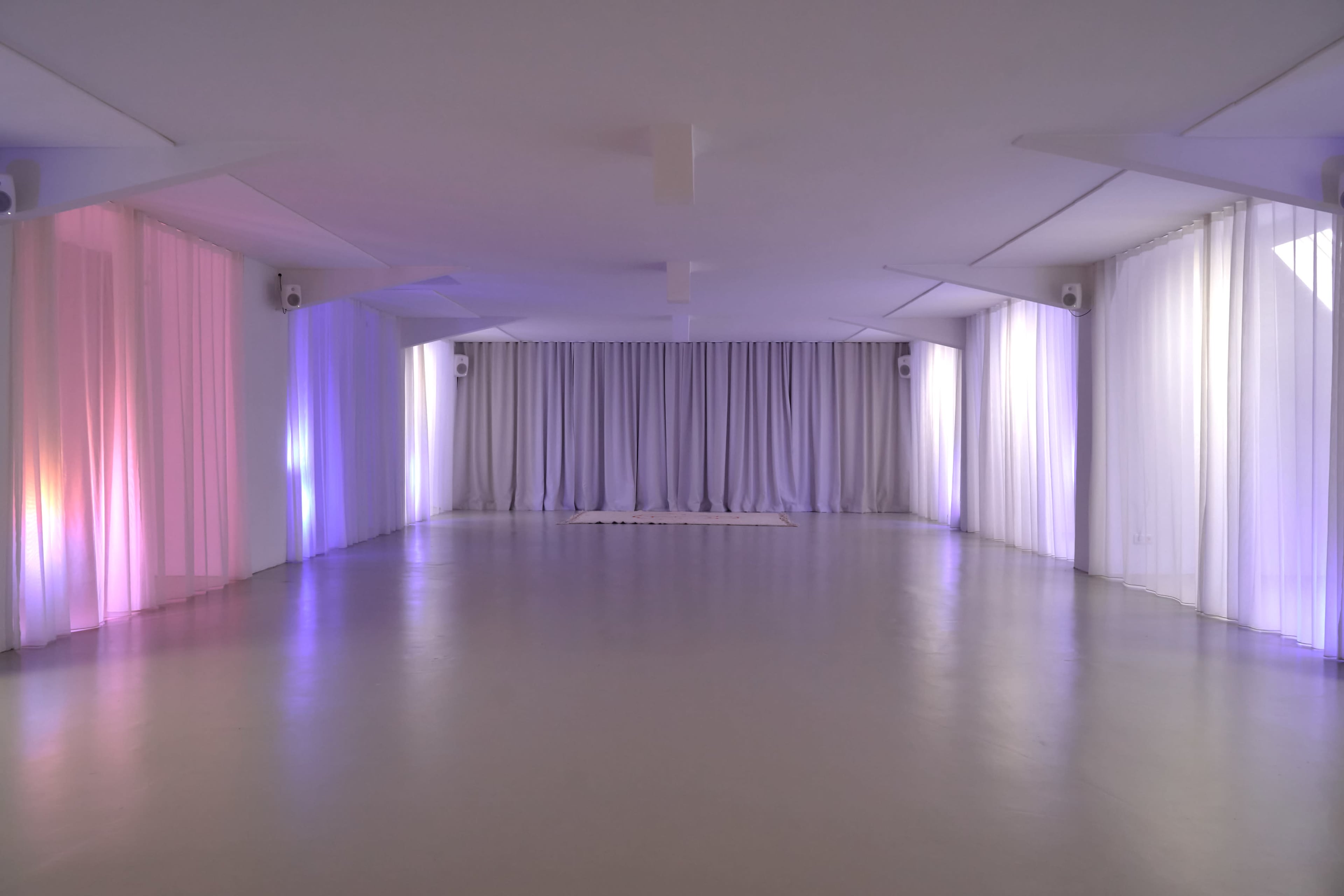 The image shows an empty, modern interior space with flowing curtains illuminated by soft, colored lights.