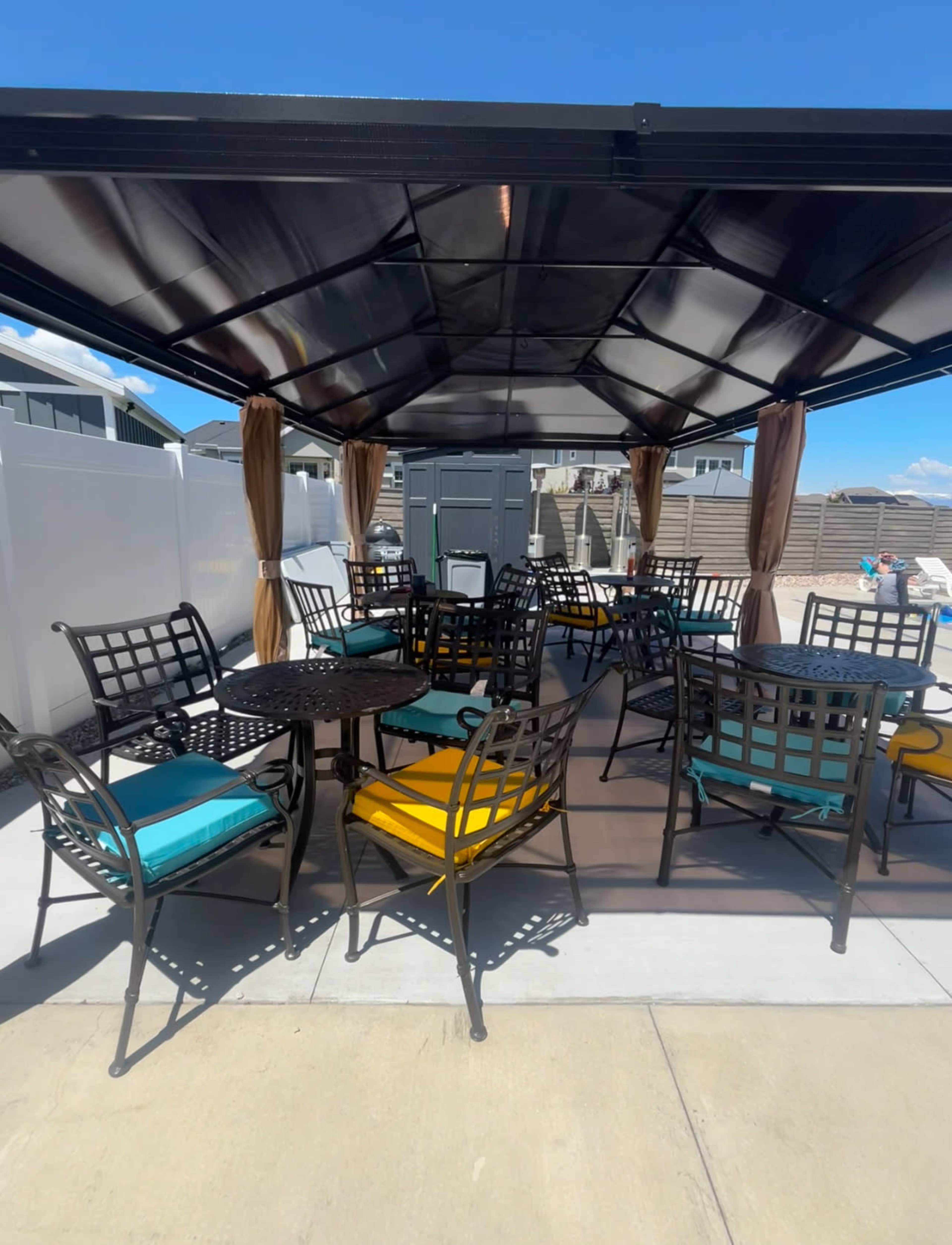 A covered outdoor seating area features several tables and chairs with colorful cushions on a paved surface.