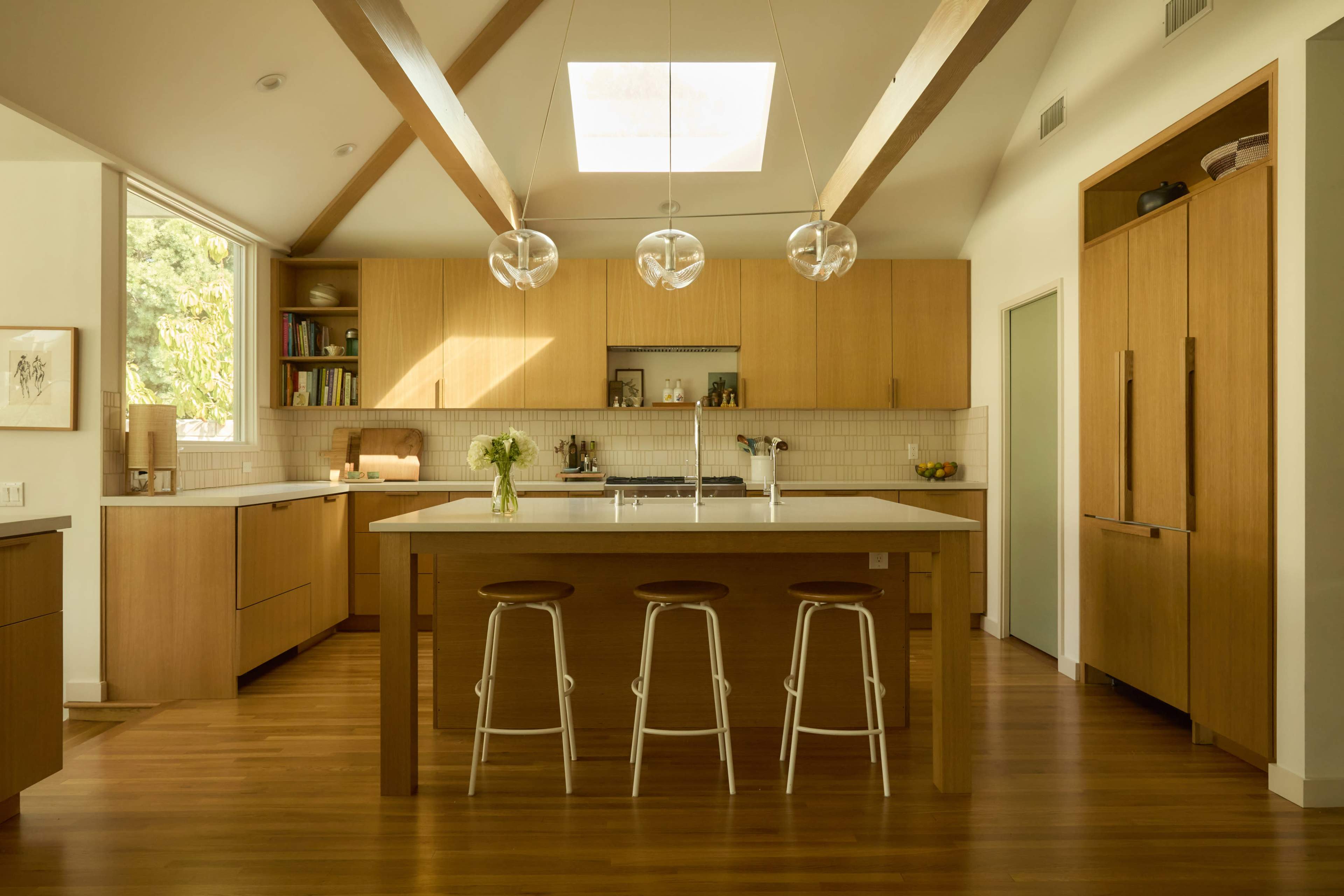 The image showcases a modern kitchen with wooden cabinetry, a large central island, and three pendant lights overhead.